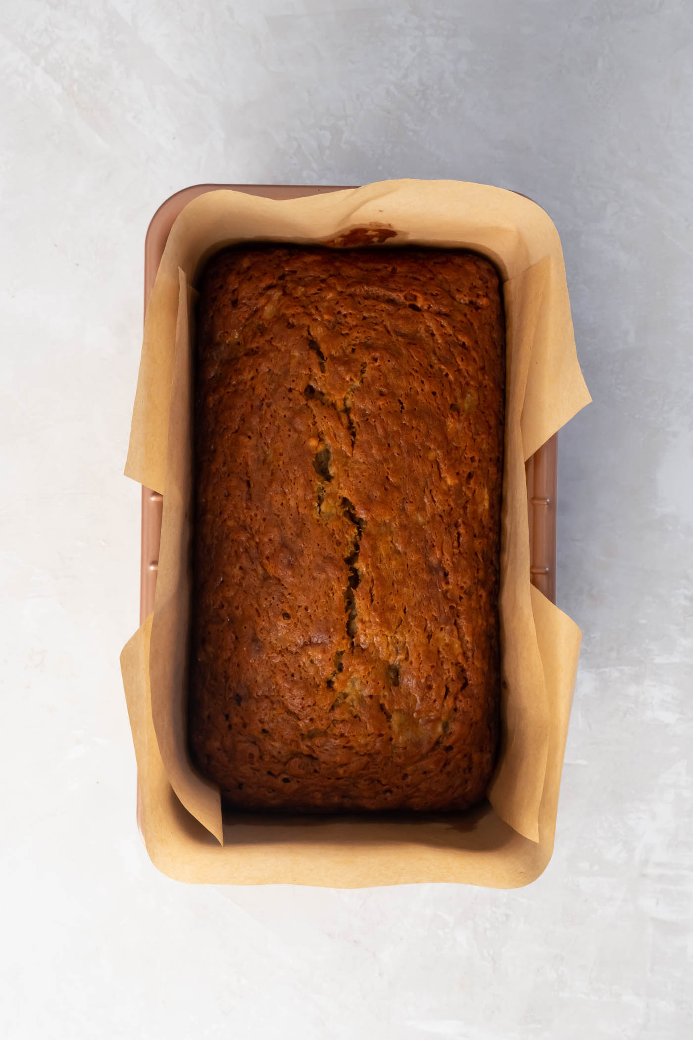 Baked loaf of banana bread in parchment paper lined metal baking pan.