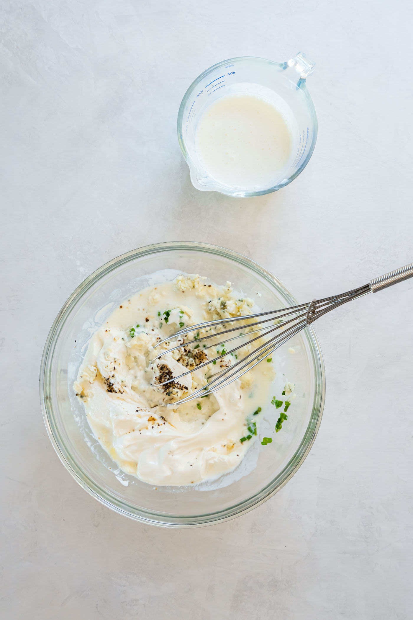 Blue cheese dressing ingredients in a mixing bowl with a whisk.