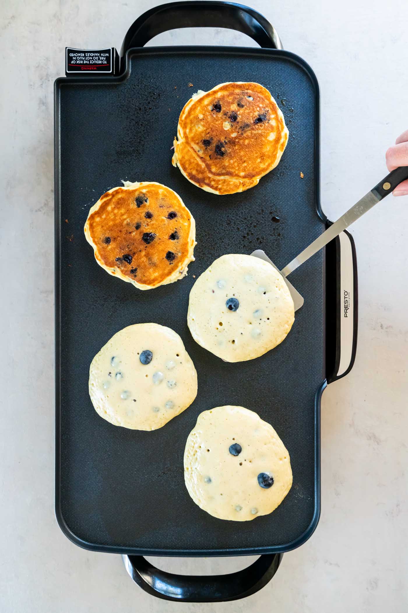 Flipping blueberry pancakes on a griddle.