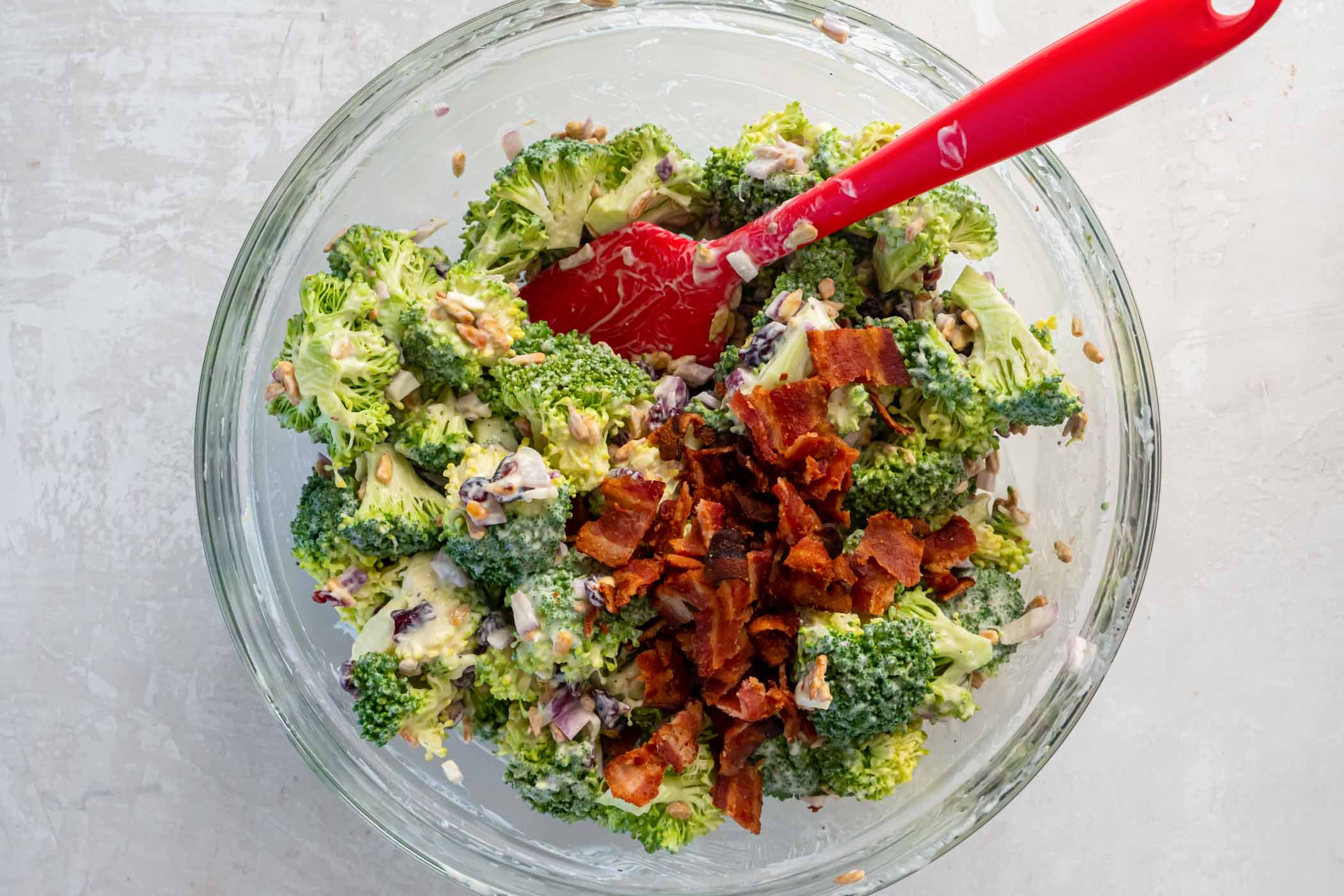 Chopped bacon added to broccoli salad in mixing bowl.