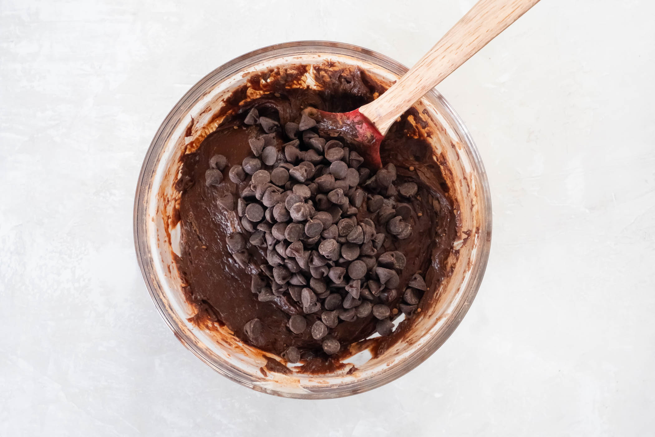 Chocolate chips added to batter in bowl with a rubber spatula.