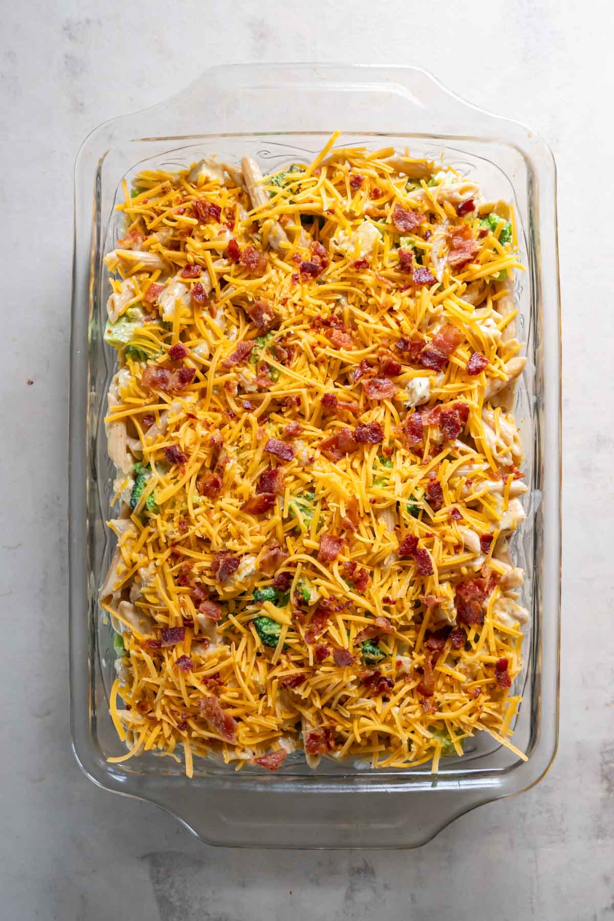 Casserole mixture in baking dish topped with cheese and bacon before baking.