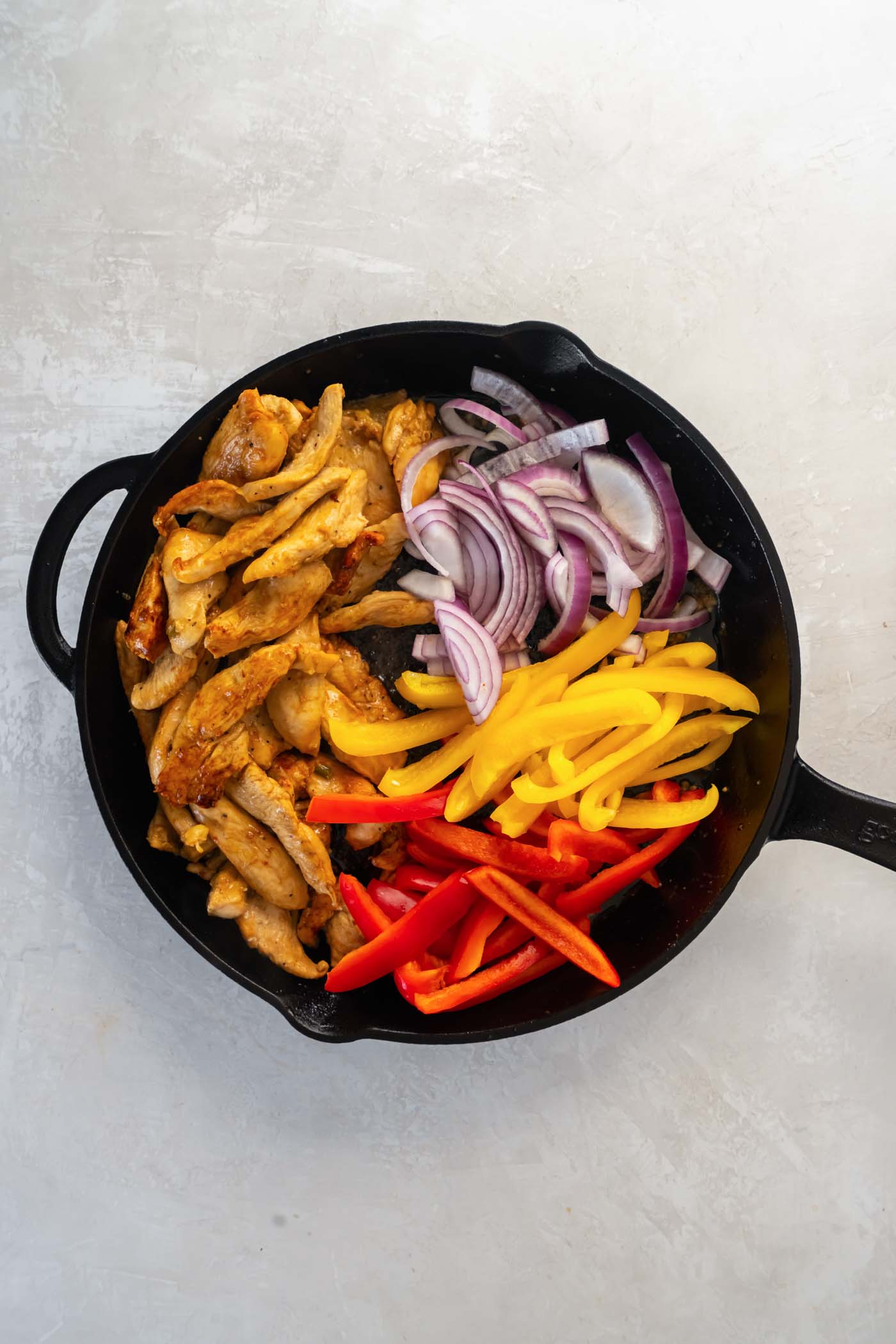 Cooking chicken strips, sliced red onion and sliced bell peppers in a cast iron skillet.