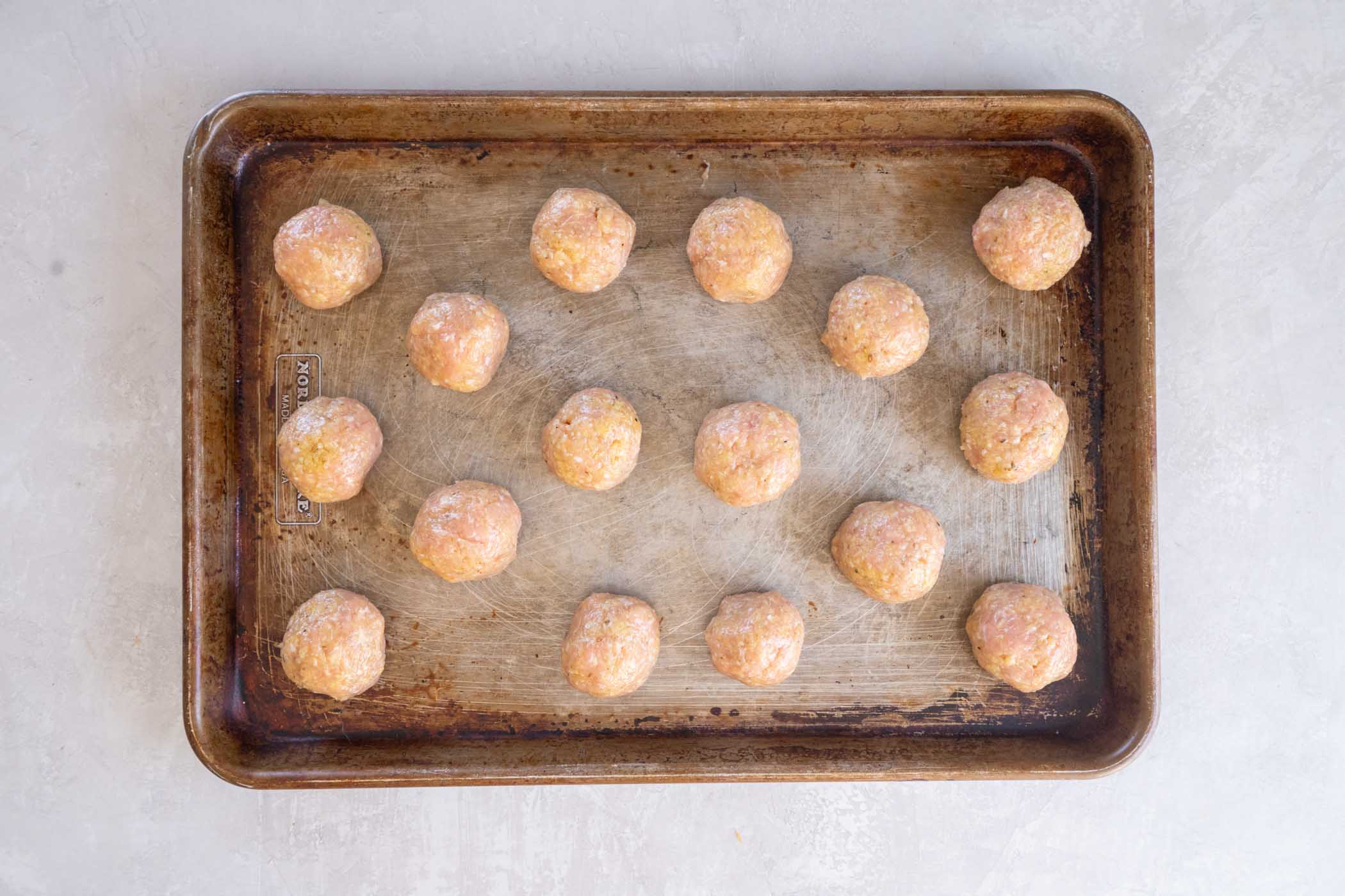 Unbaked chicken meatballs on a greased baking sheet.
