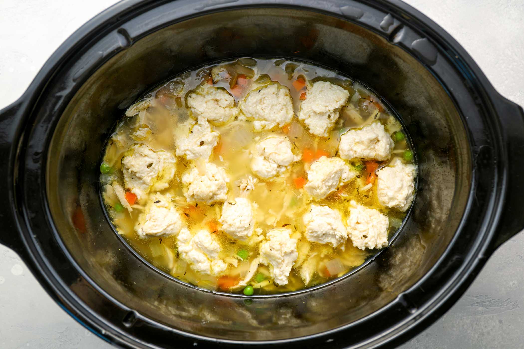 Spoonfuls of dumpling dough added on top of chicken soup in slow cooker.