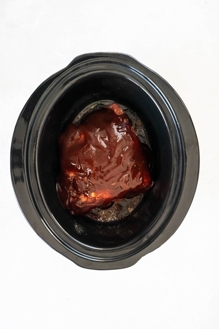 Uncooked pork butt with seasonings, bbq sauce and apple cider vinegar in slow cooker.