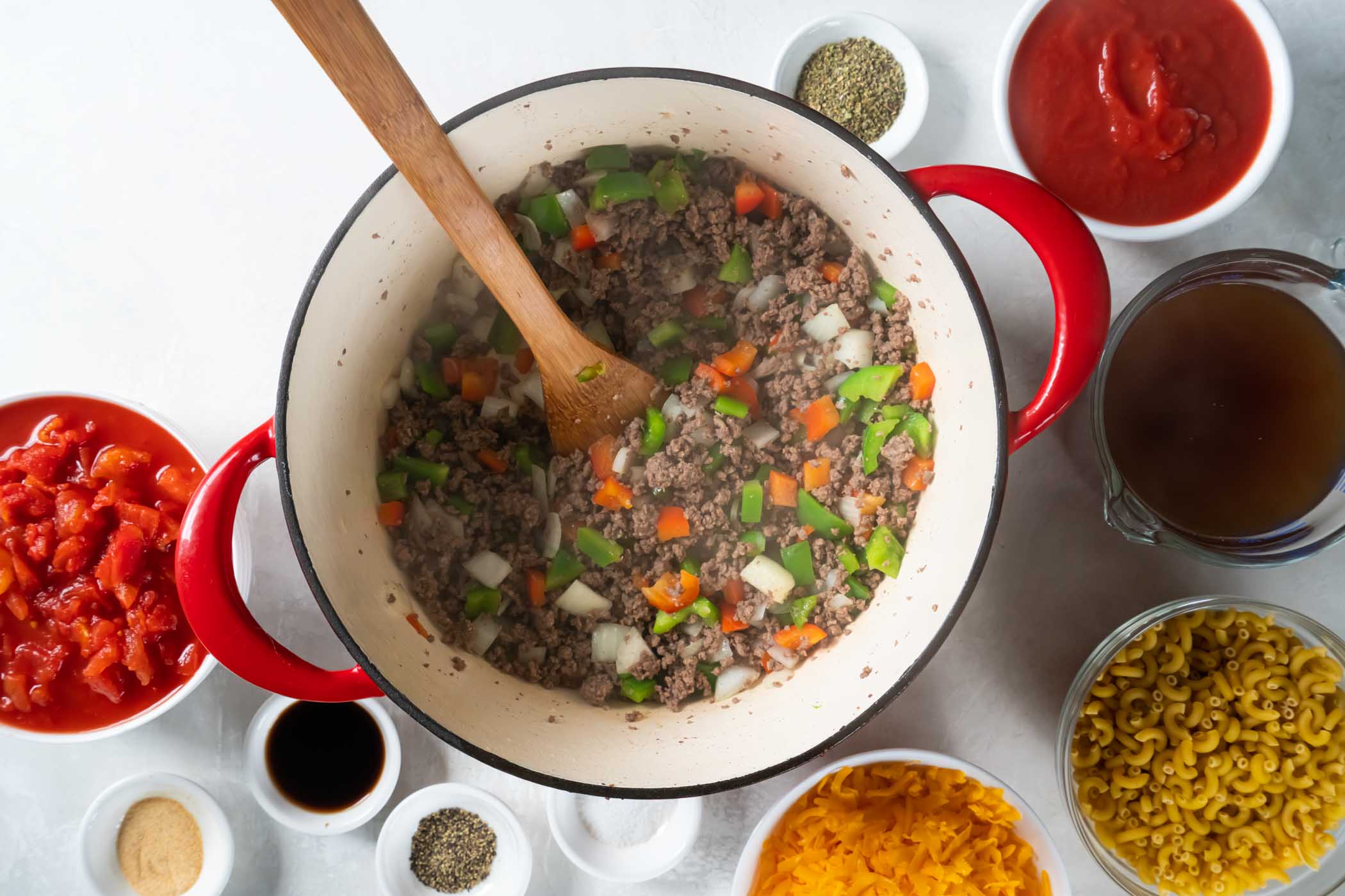 Browned ground beef and sautéed peppers and onions in pot with wooden spoon.