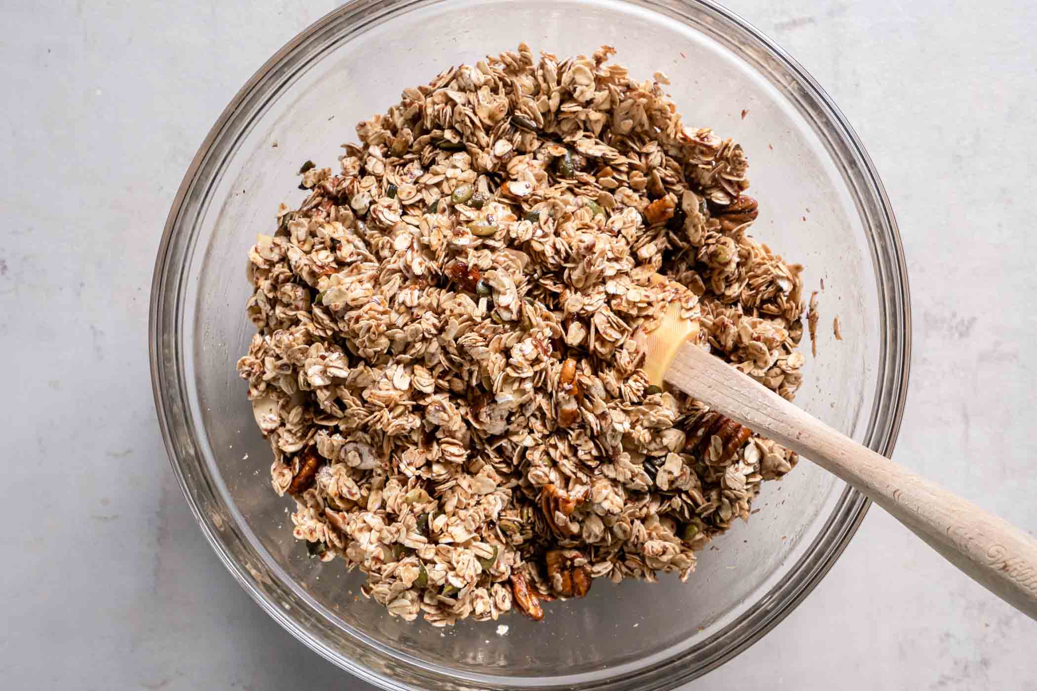 Granola in mixing bowl with a rubber spatula.