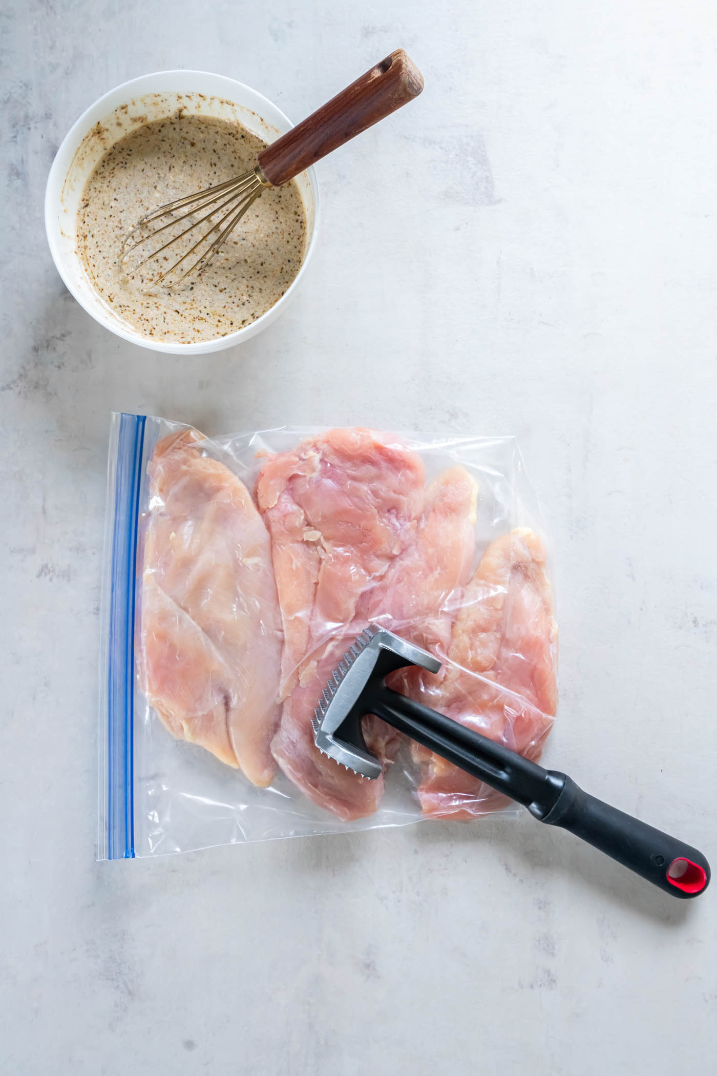 Pounding chicken breasts in zip-top bag with meat mallet.