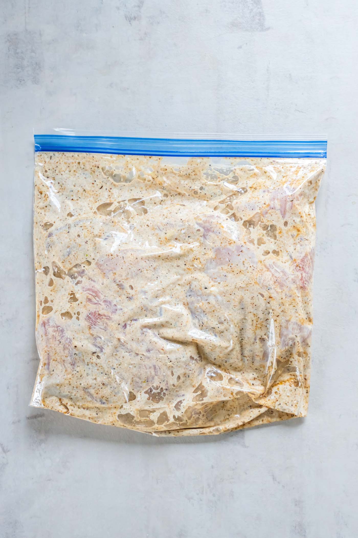 Chicken breasts and Greek chicken marinade in a zip-top bag.