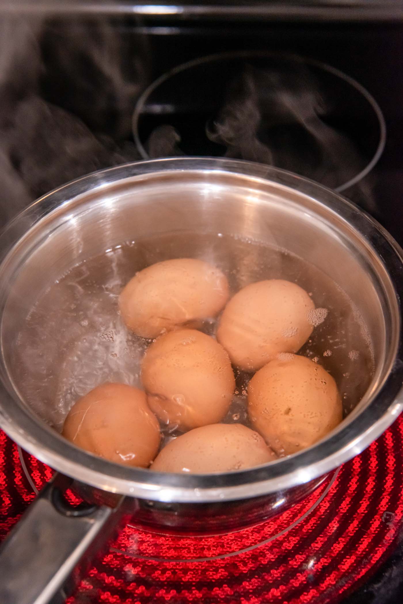 Eggs boiling in pot of water on the stove.