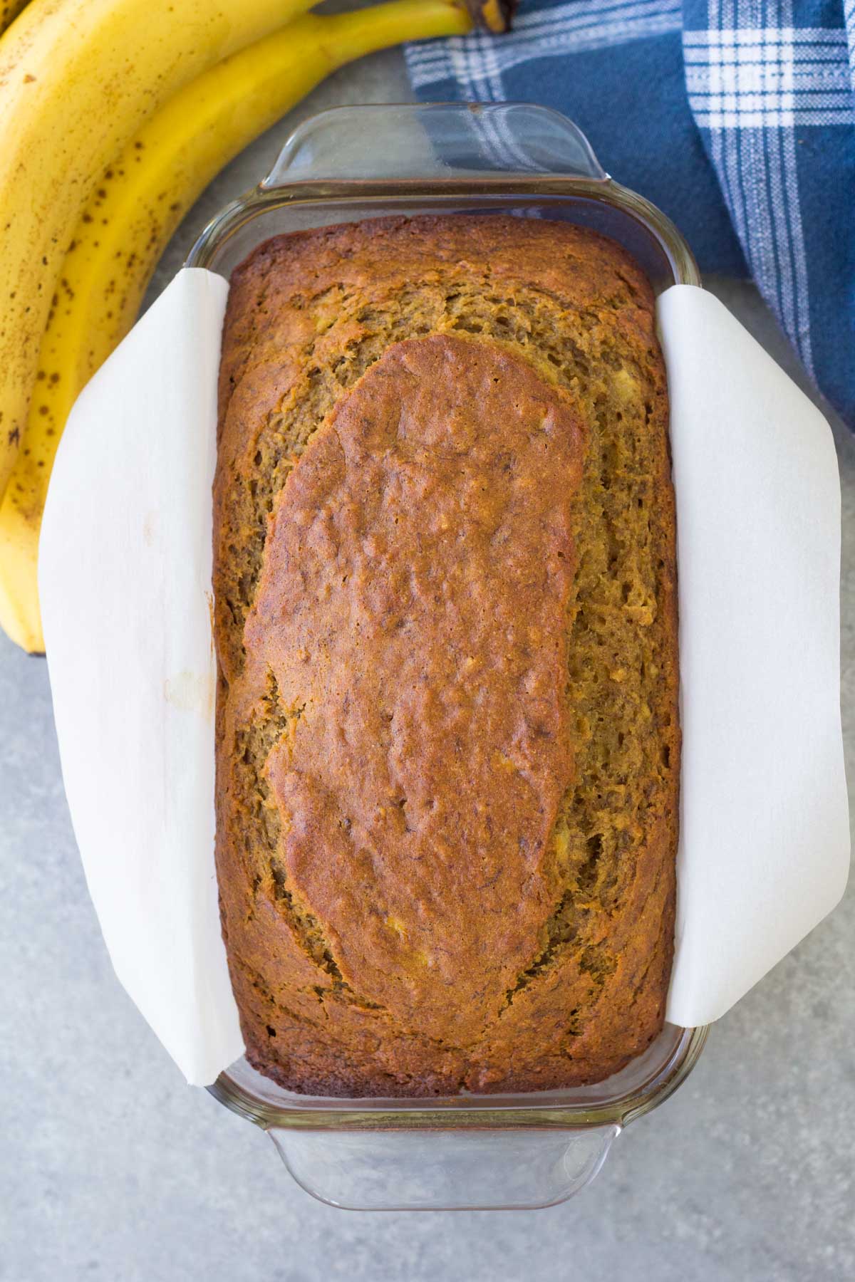Baked loaf of banana bread in glass loaf pan lined with parchment paper.