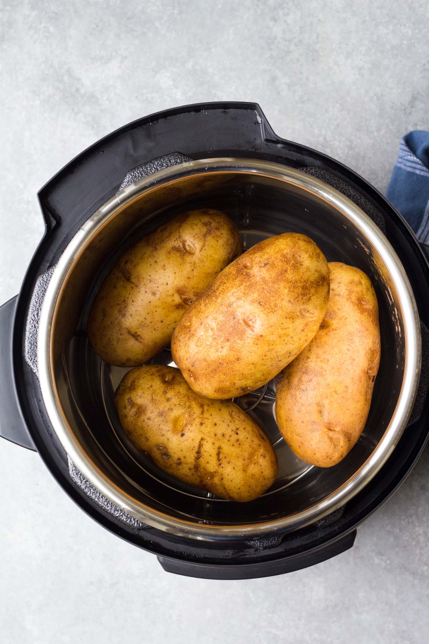 Four uncooked russet potatoes on trivet in instant pot.