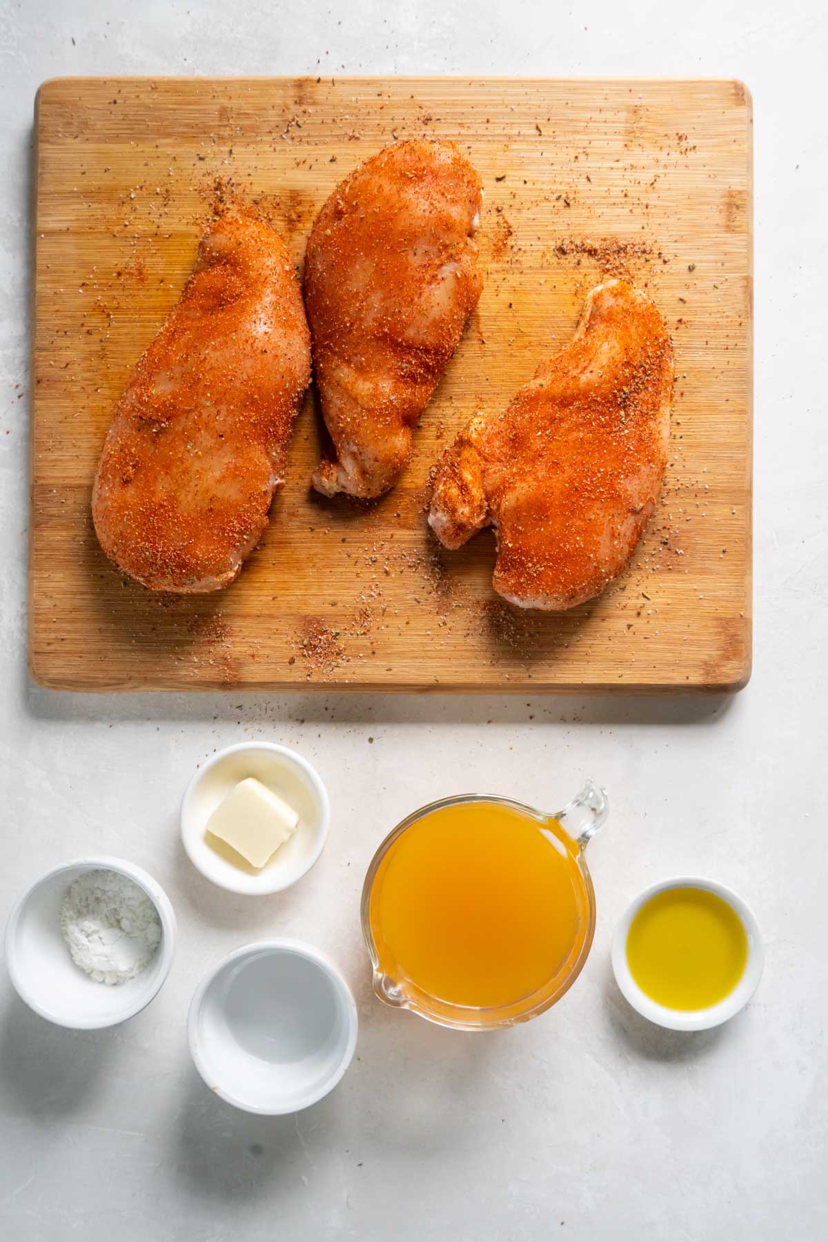 Seasoned raw chicken breasts on a cutting board.