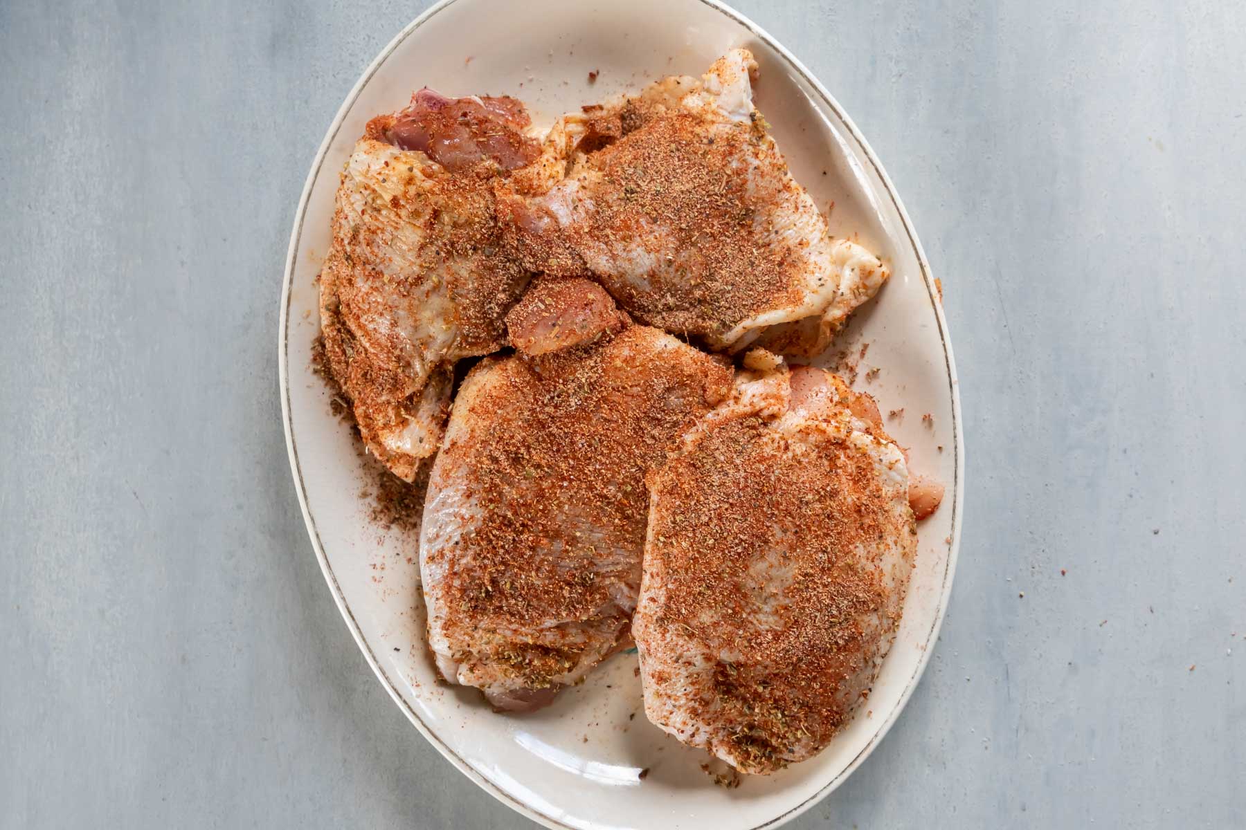 Seasonings rubbed onto 4 bone-in chicken thighs on a plate.