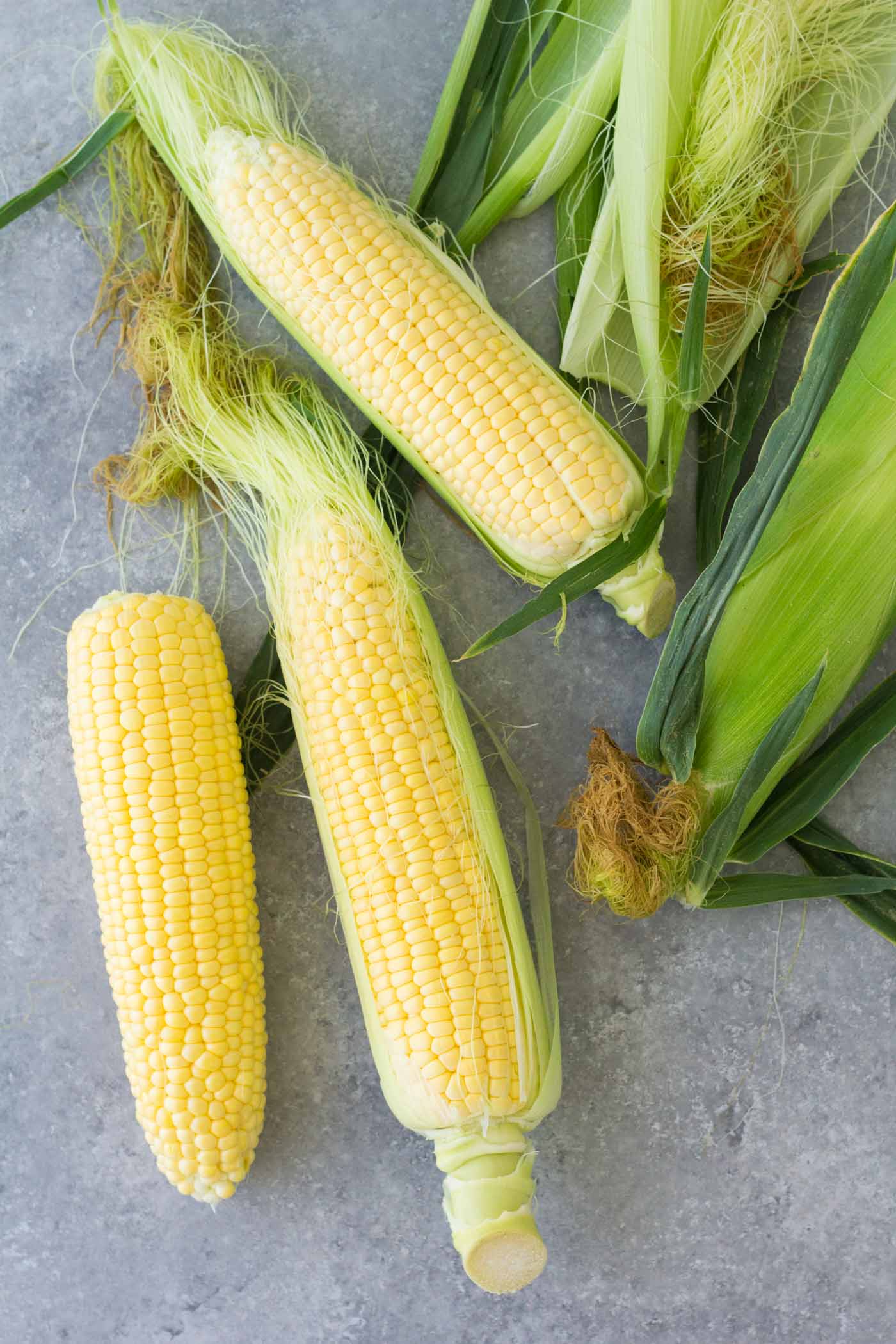 Three cobs of partially shucked corn on the cob.