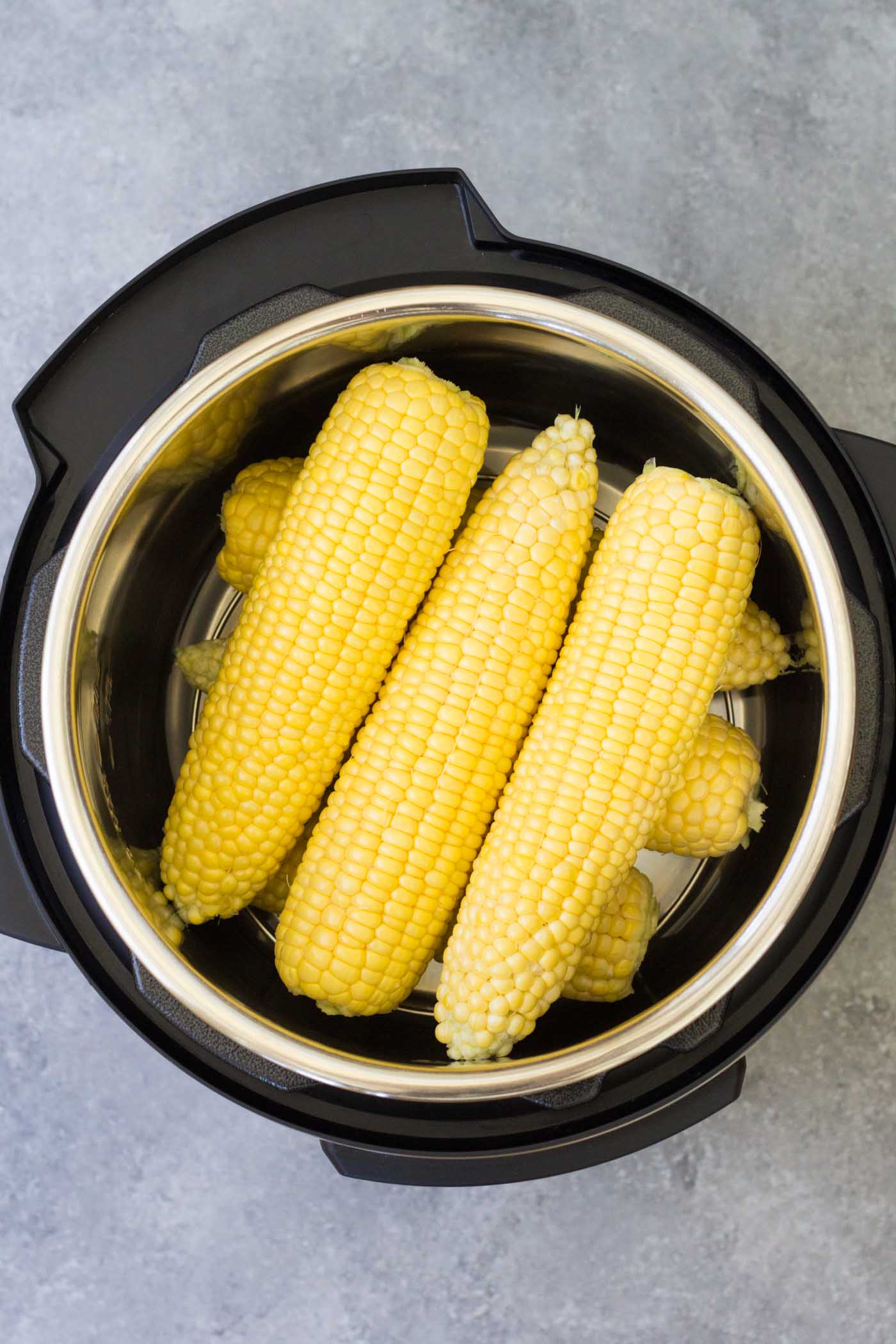 Six ears of uncooked corn on the cob in an instant pot, stacked in alternating directions with 3 ears in each layer.