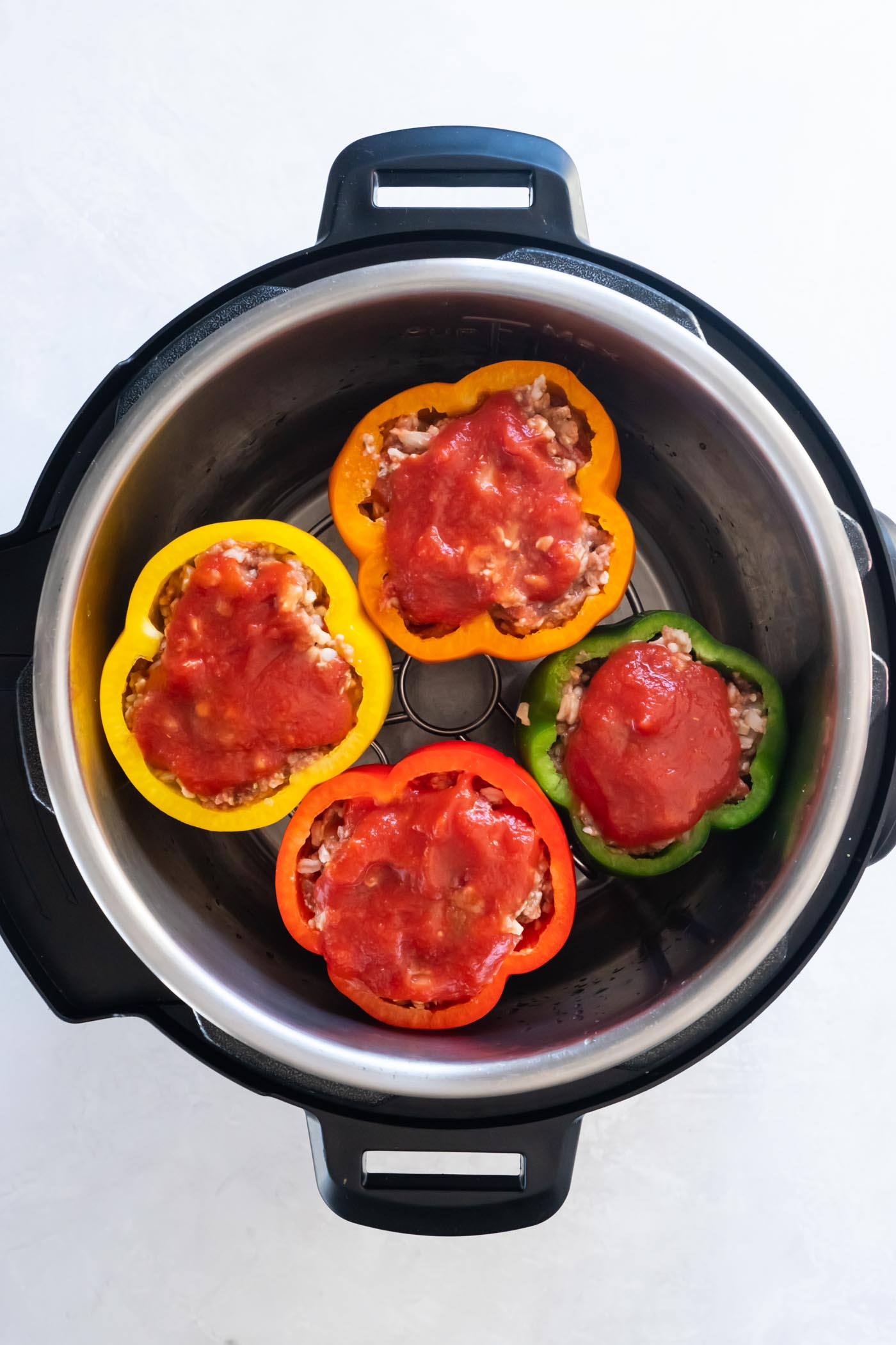 Uncooked stuffed peppers in instant pot with tomato sauce on top.