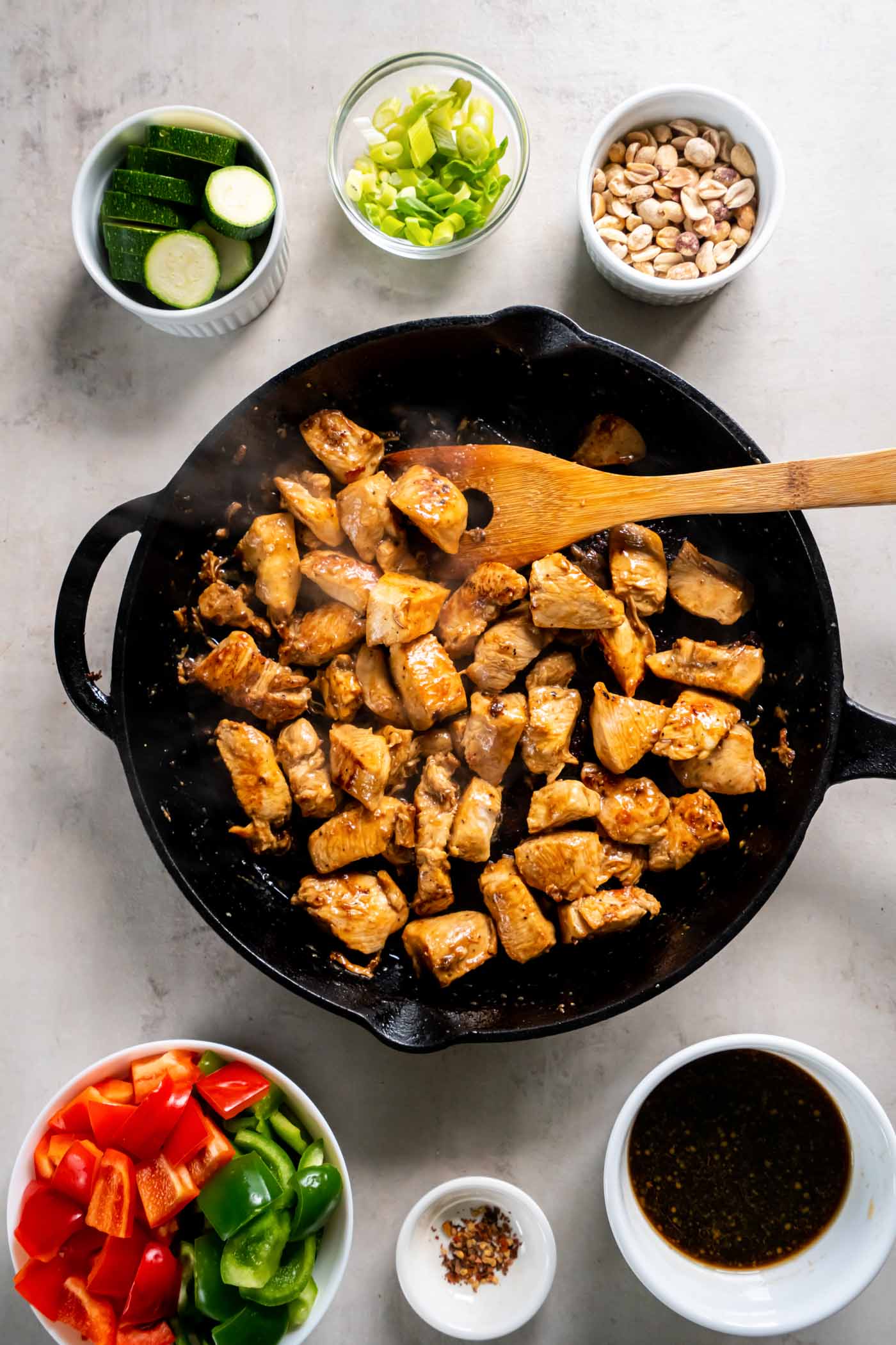 Cooked chicken pieces in skillet with a wooden spoon.