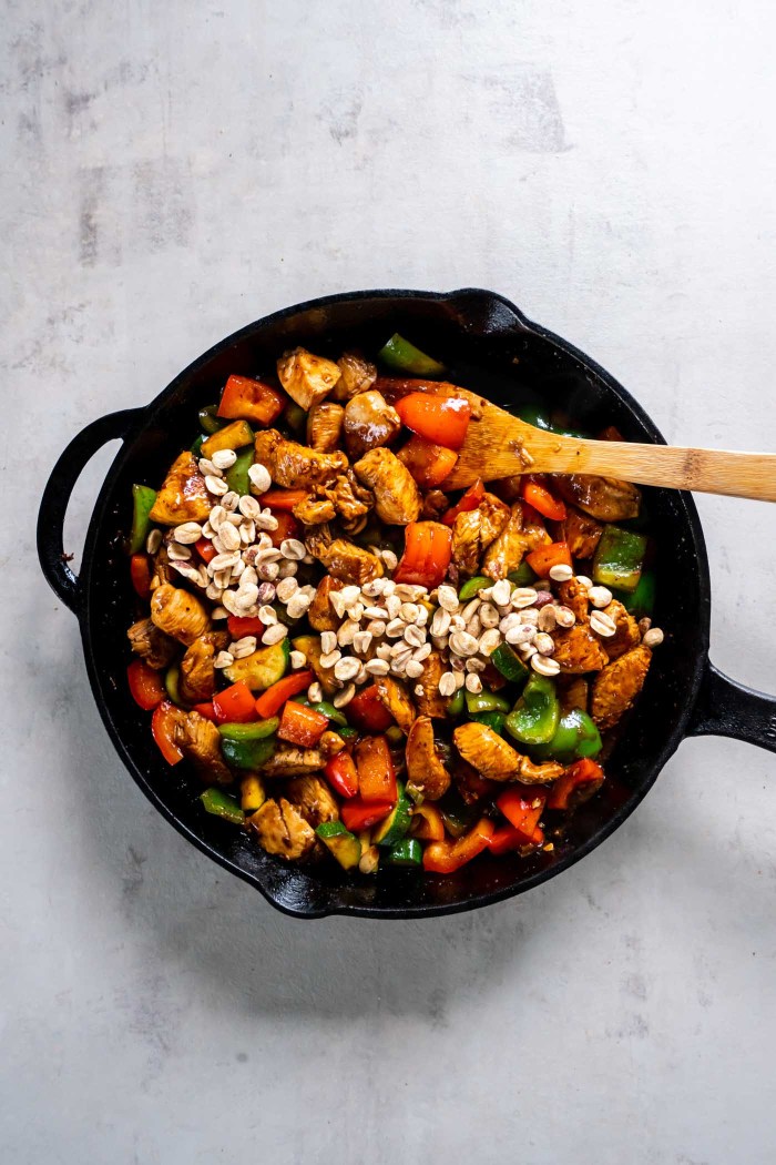 Peanuts added to kung pao chicken in skillet.
