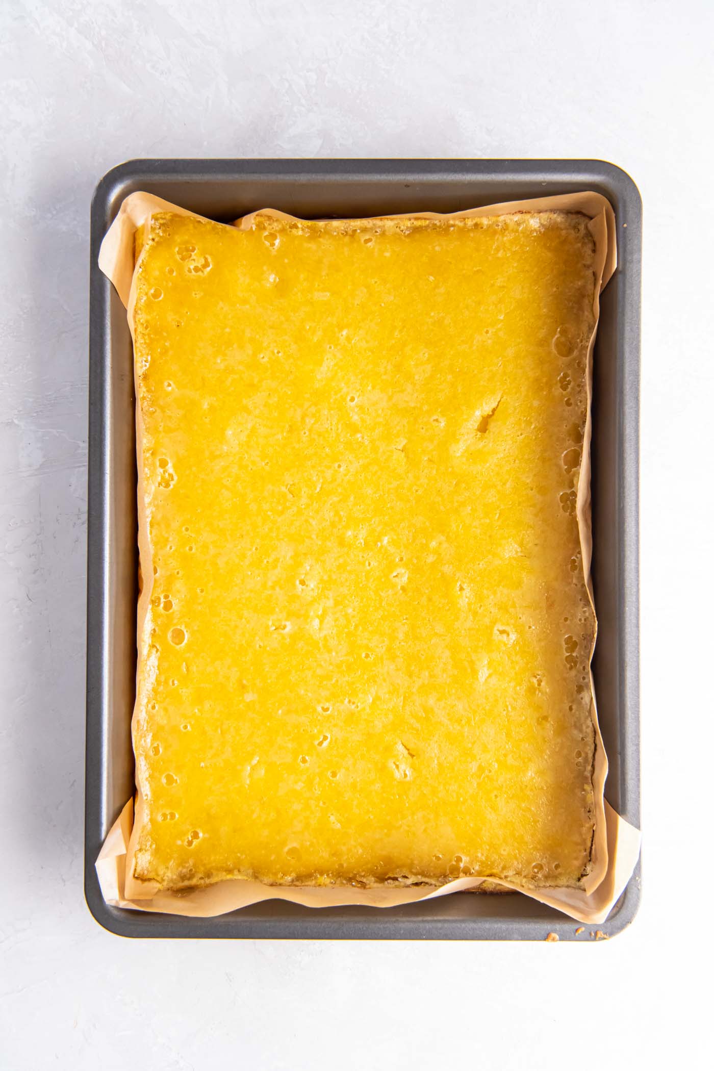 Baked lemon bars in parchment lined metal baking pan.