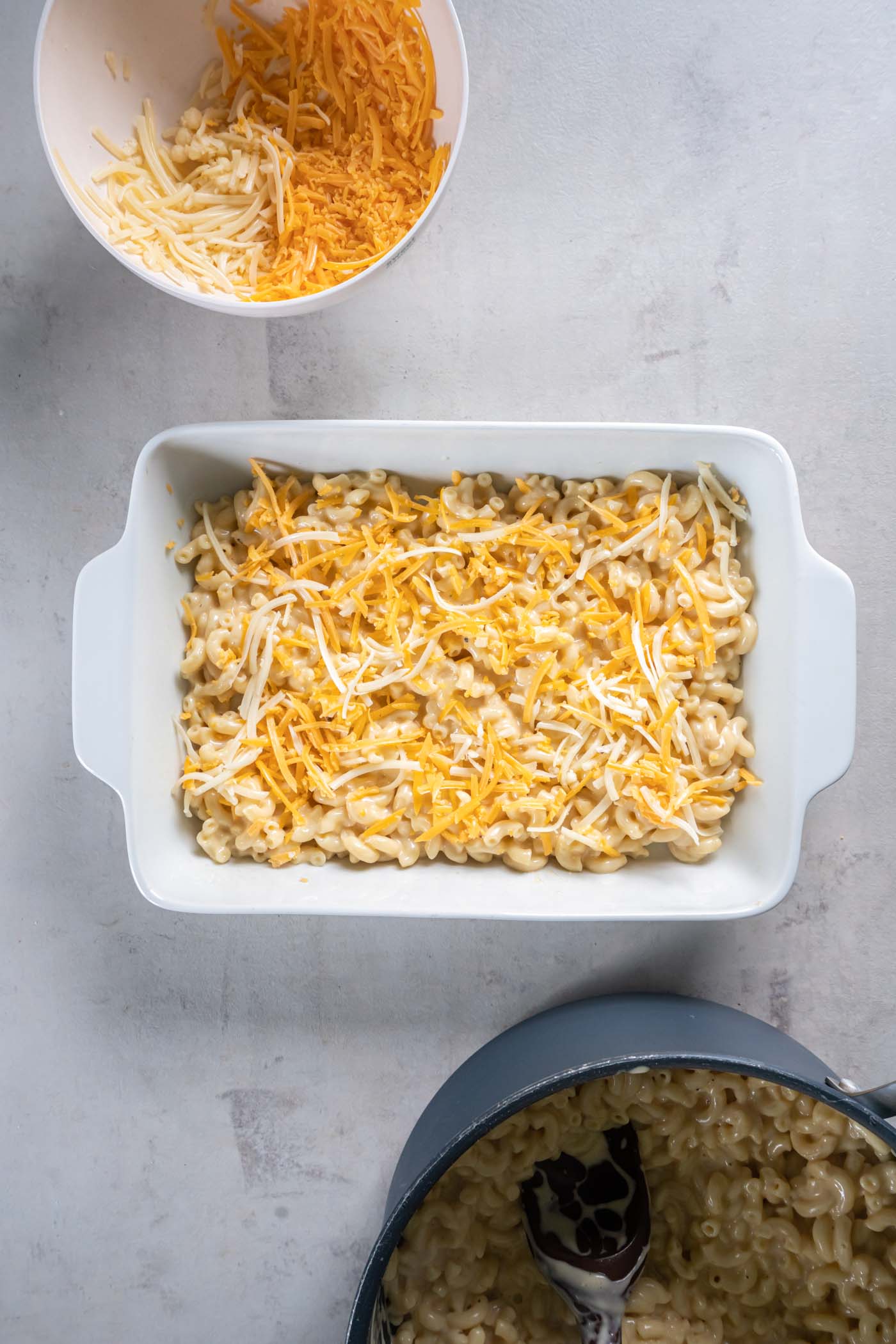 Cheesy pasta layer in baking dish with shredded cheese on top.
