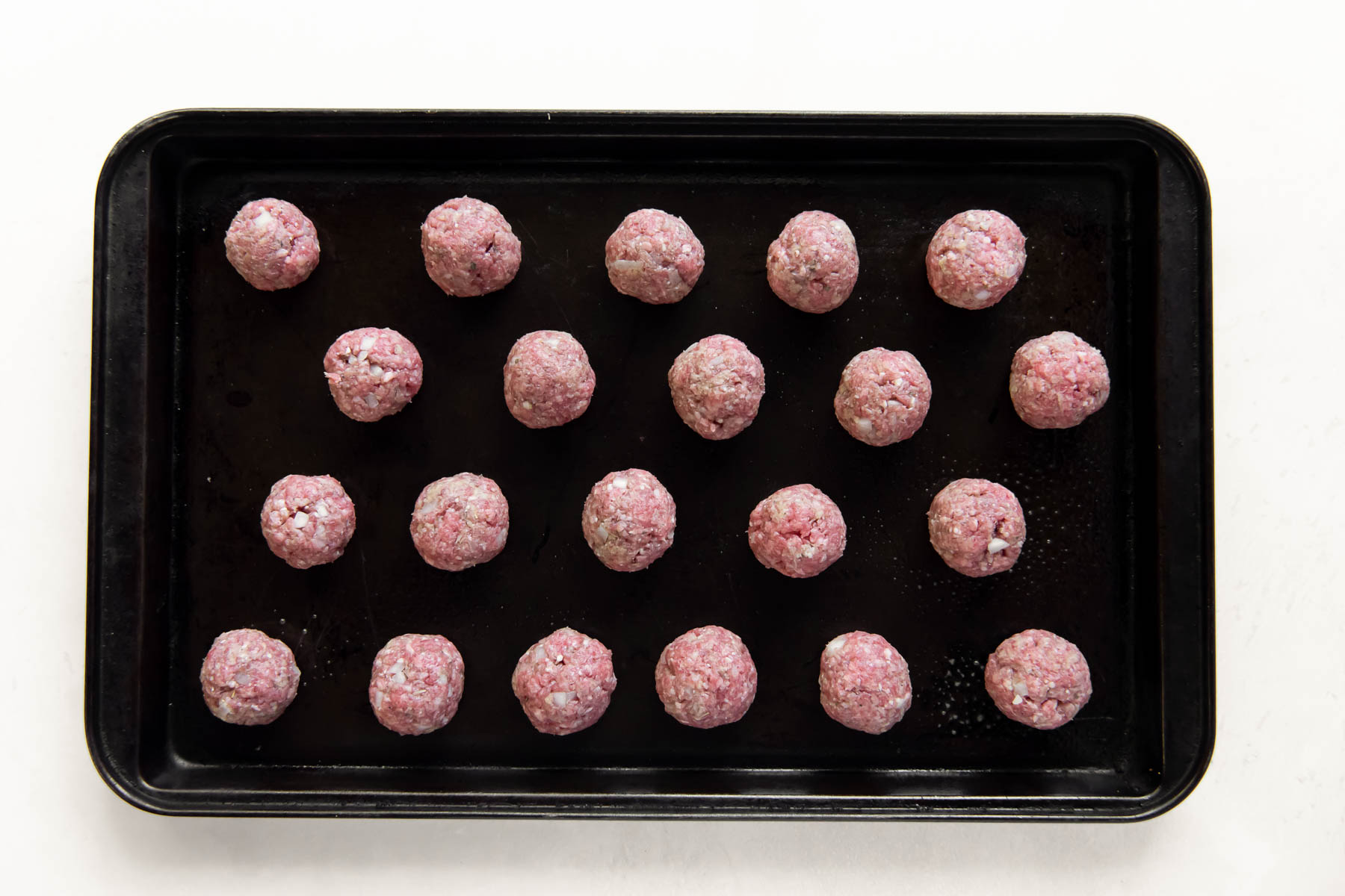 unbaked meatballs on a rimmed baking sheet