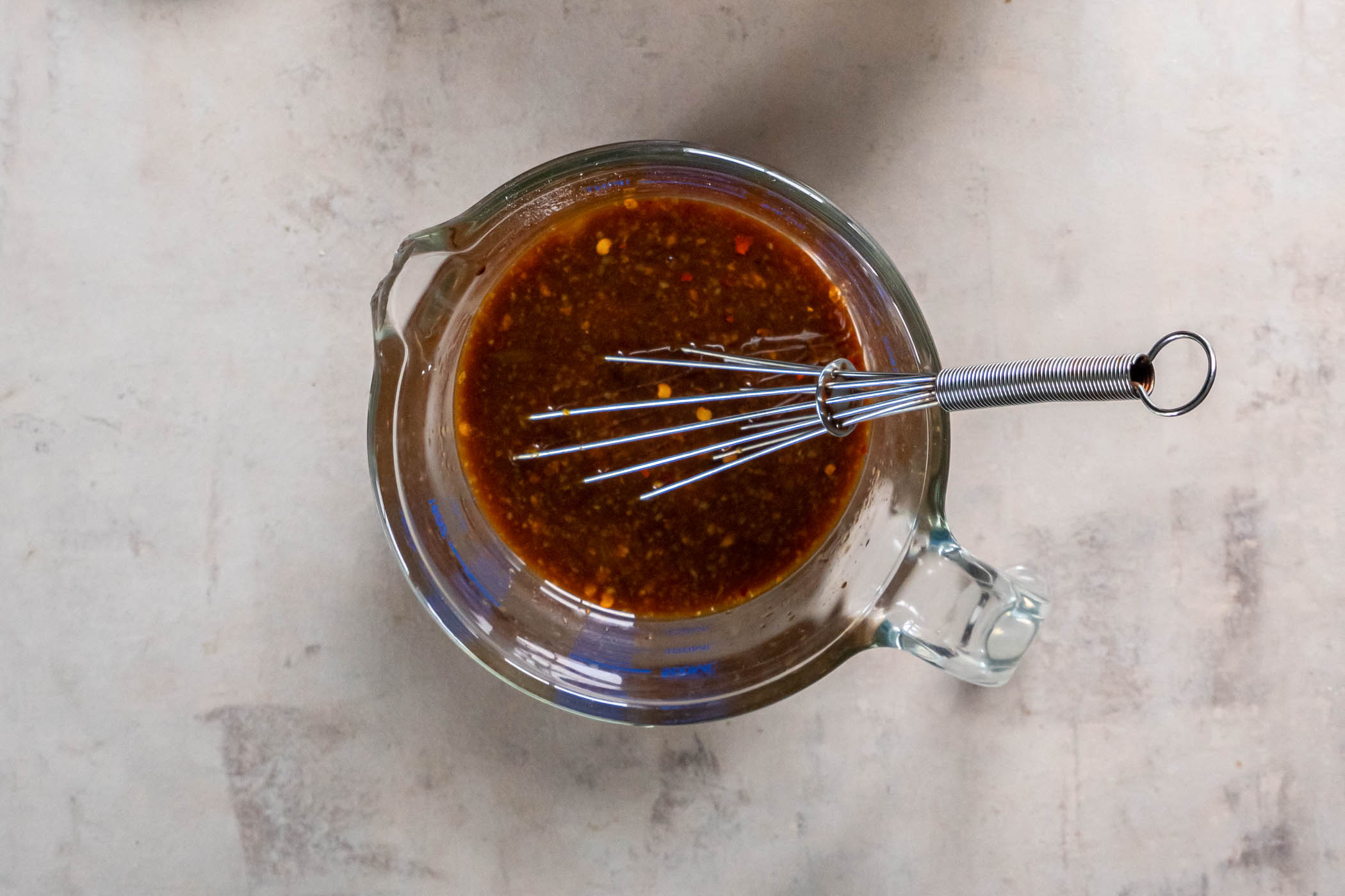 Orange chicken sauce in a liquid measuring cup with a whisk.