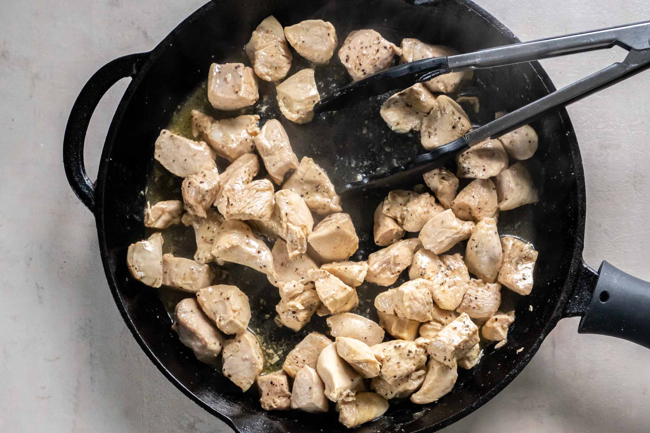 Cooking chicken pieces in a cast iron skillet.