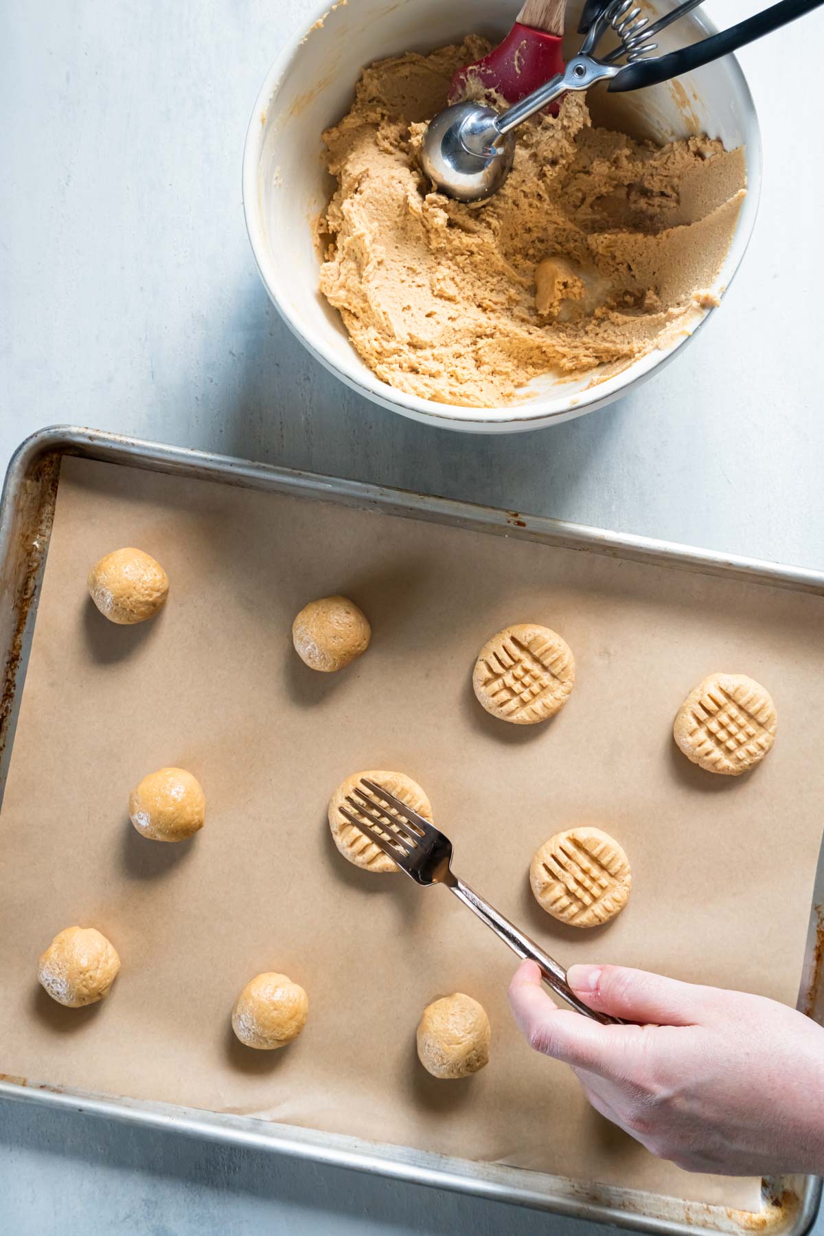 Making crisscross pattern on cookie dough balls on baking sheet with a fork.