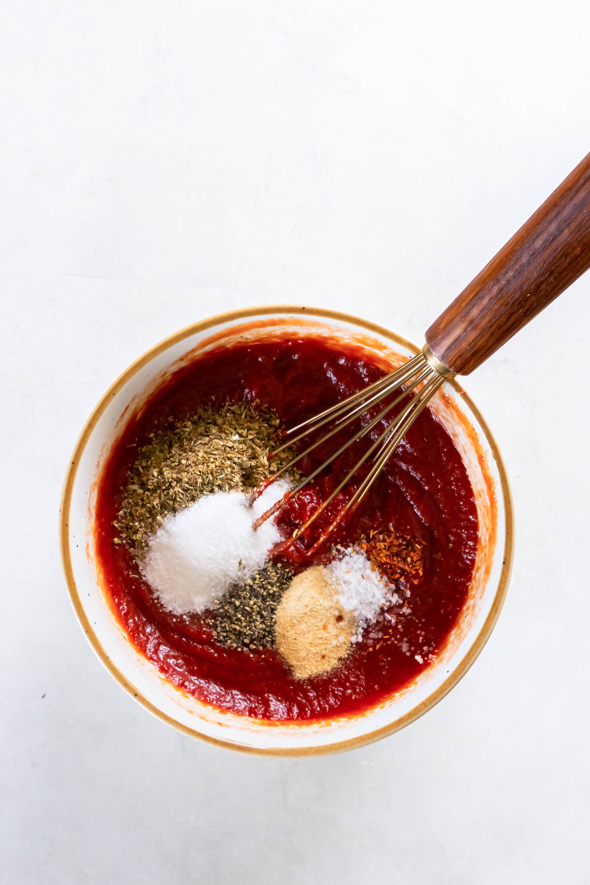 Seasonings added to pizza sauce in bowl with whisk.