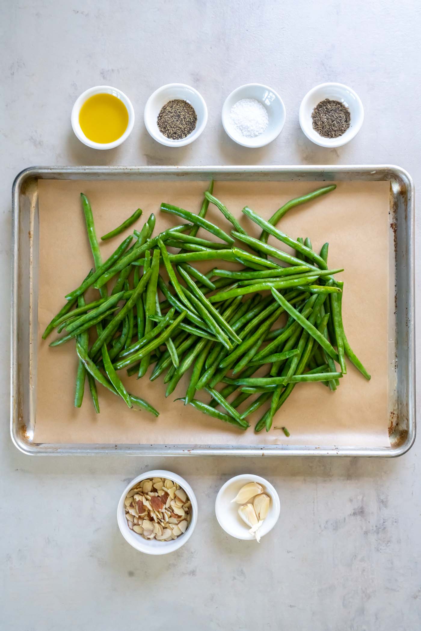 Trimmed green beans on a parchment paper lined baking sheet with other recipe ingredients around the baking sheet.