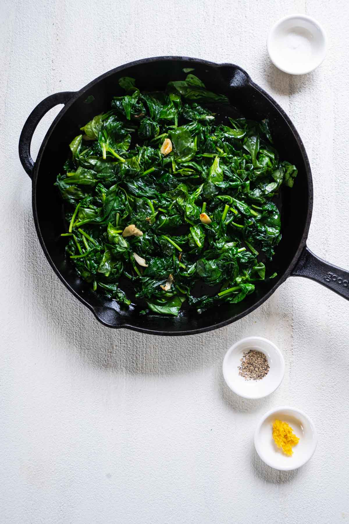 Sauteed spinach with smashed garlic cloves in skillet.