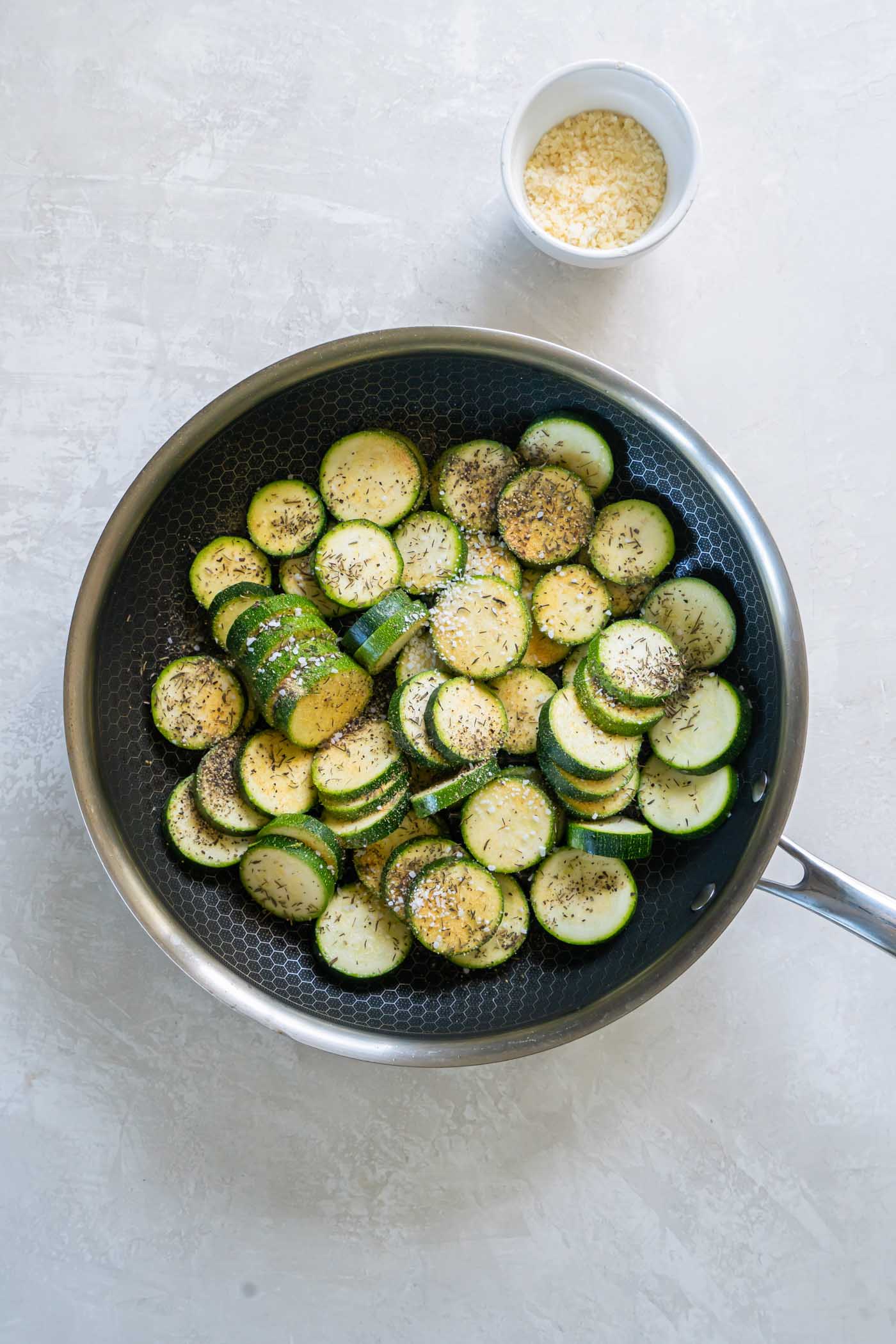 Zucchini rounds with seasonings sprinkled over them in skillet.