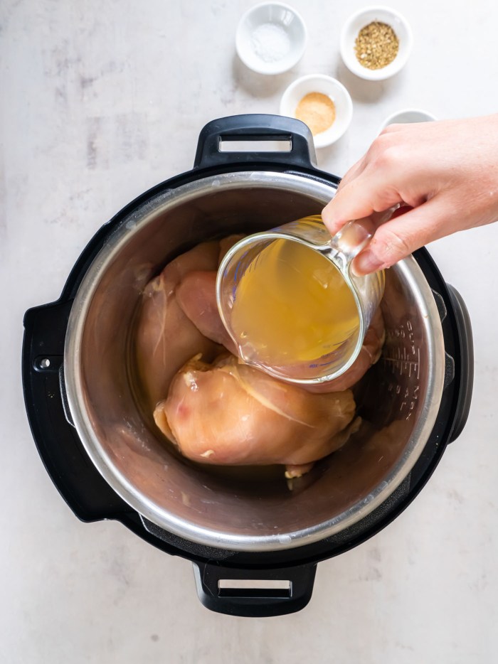 Pouring chicken broth over raw chicken breasts in Instant Pot.