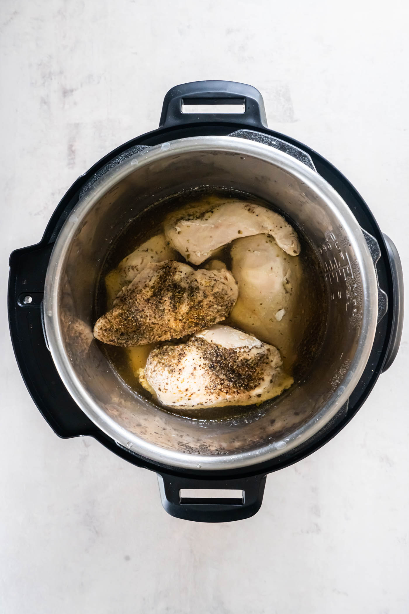 Cooked chicken breasts with broth and seasonings in Instant Pot.