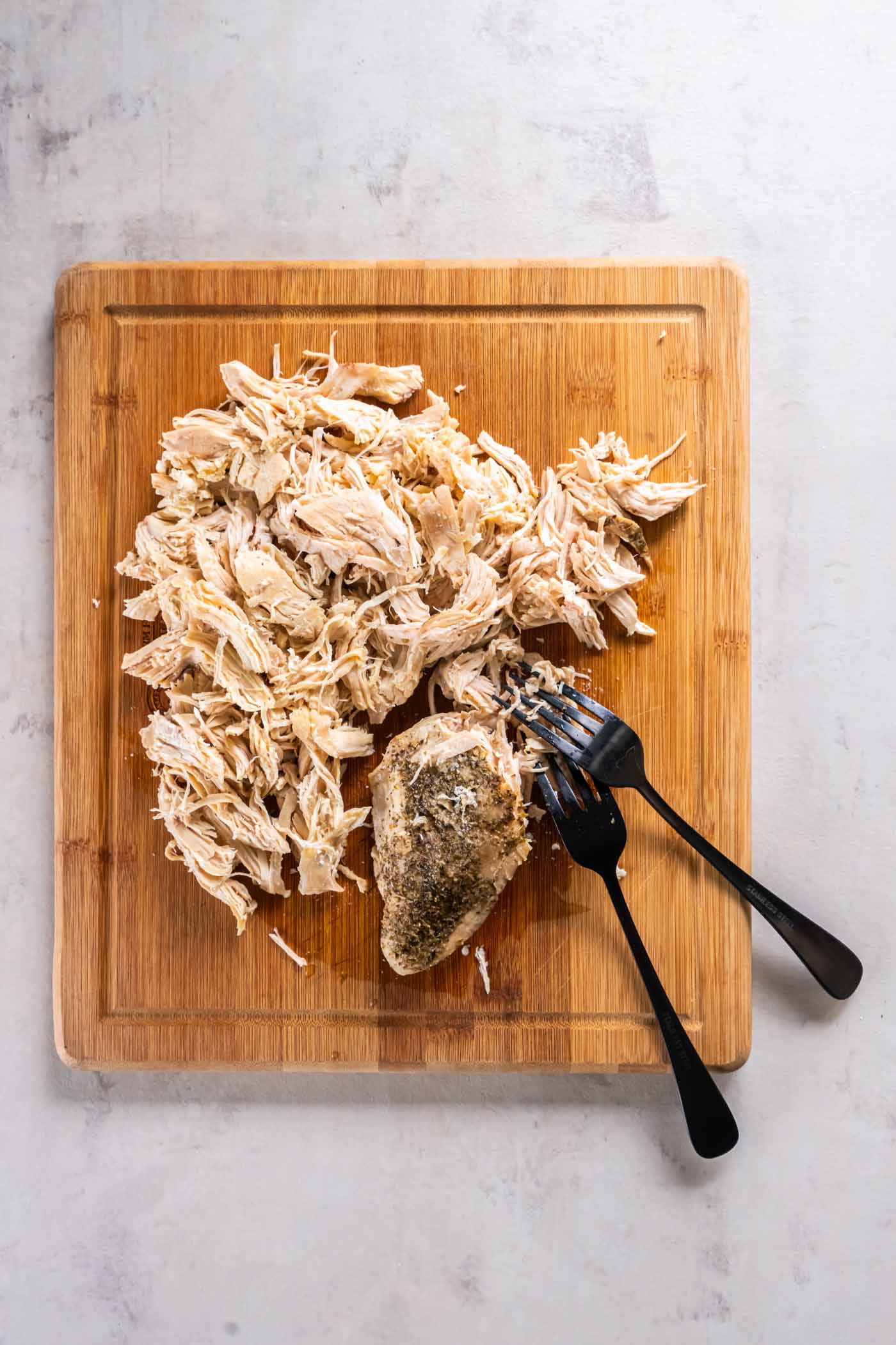 Shredding chicken breasts with two forks on a cutting board.