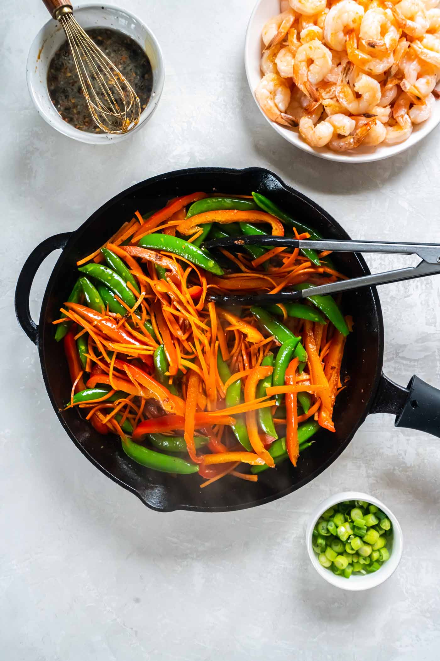 Stir frying carrots, bell peppers and snap peas in a skillet.