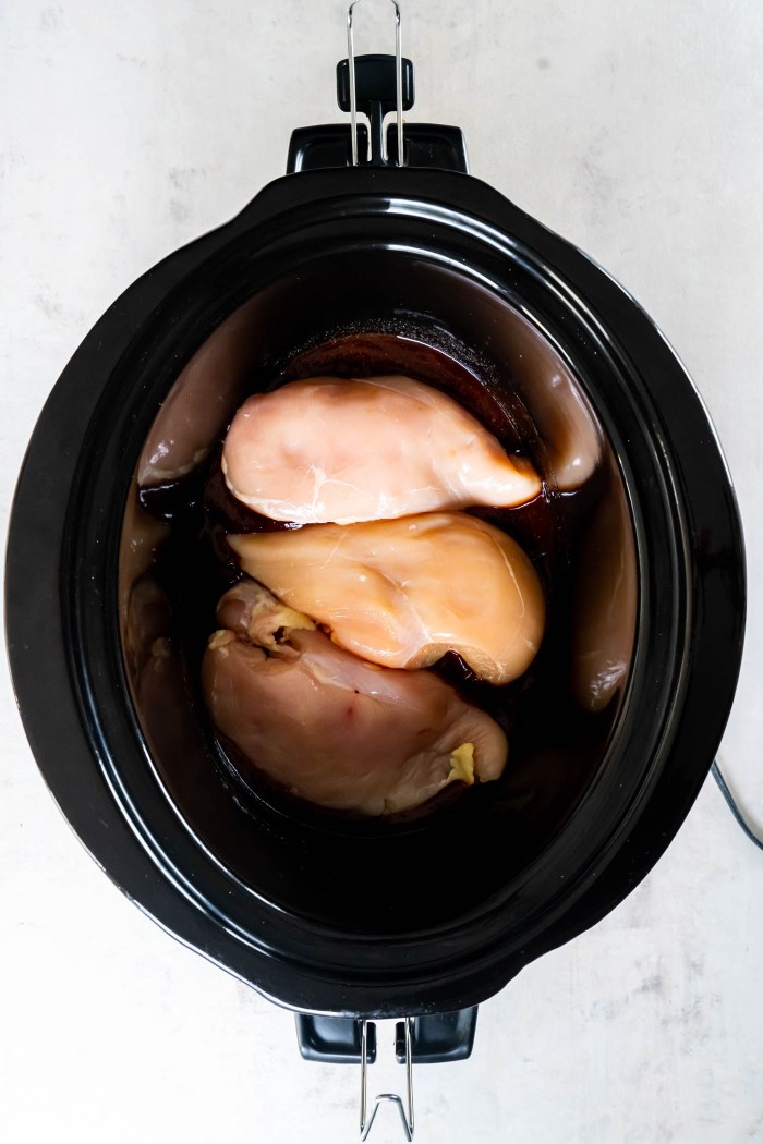 Three raw chicken breasts in bbq sauce in slow cooker.