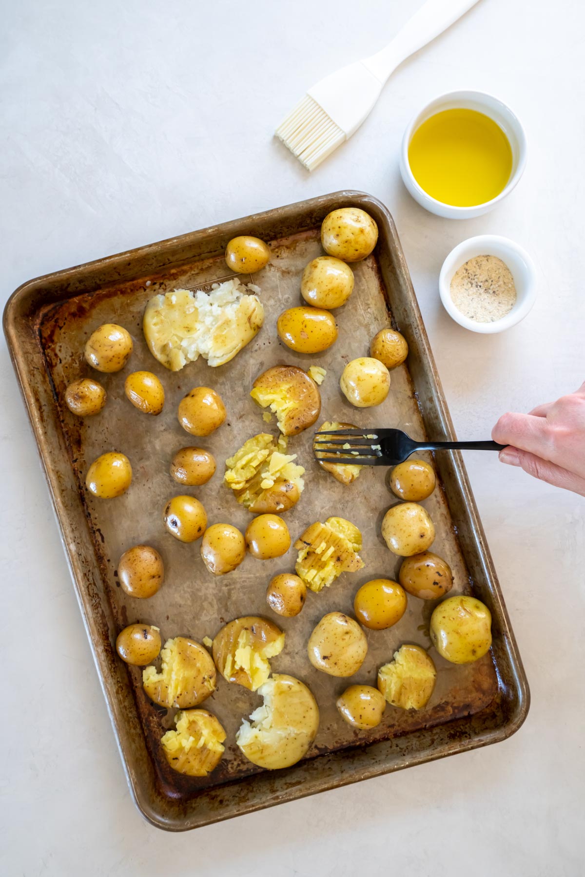 Smashing potatoes on baking sheet with a fork.