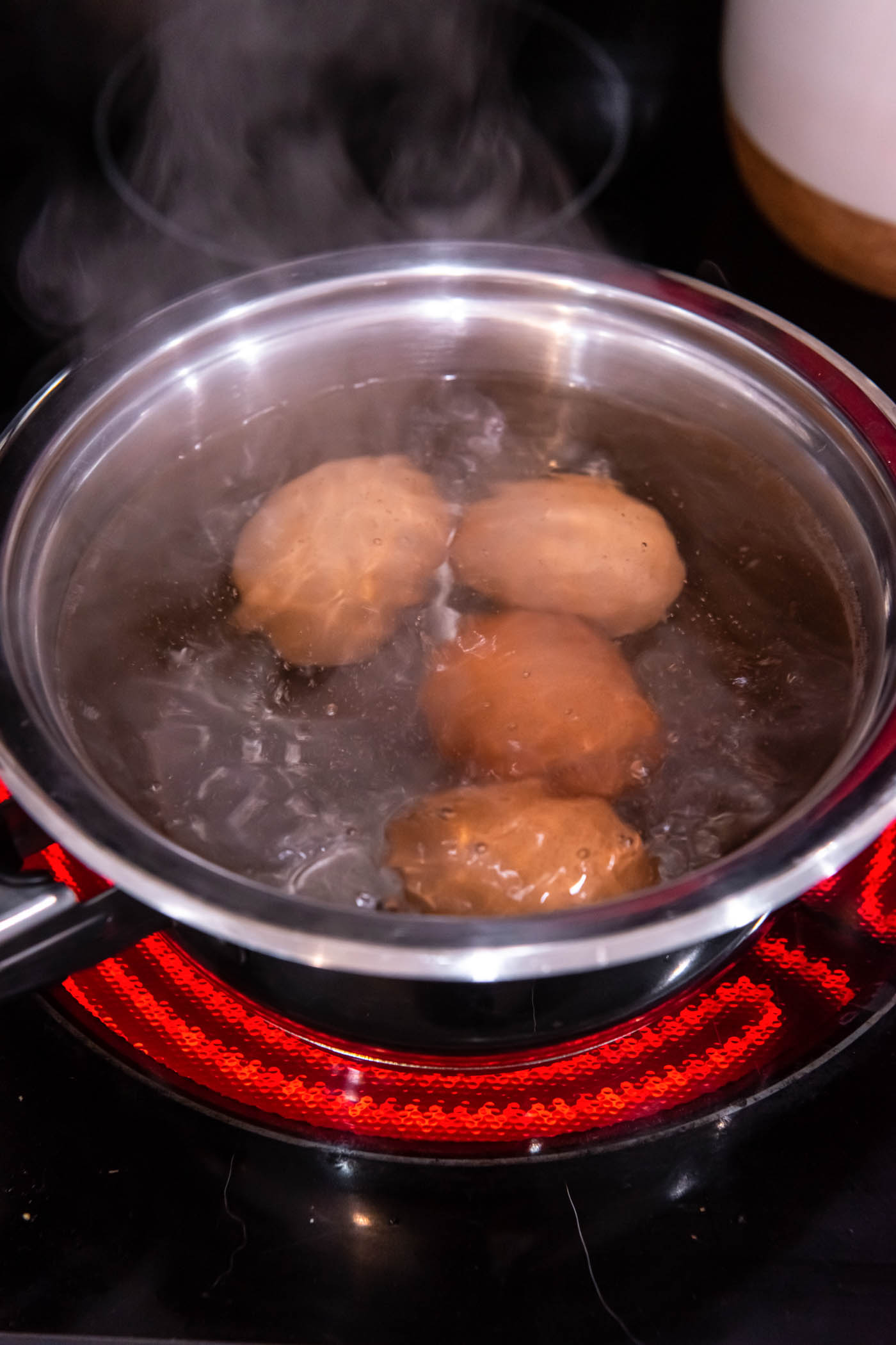 Four eggs in pot of boiling water on the stove.