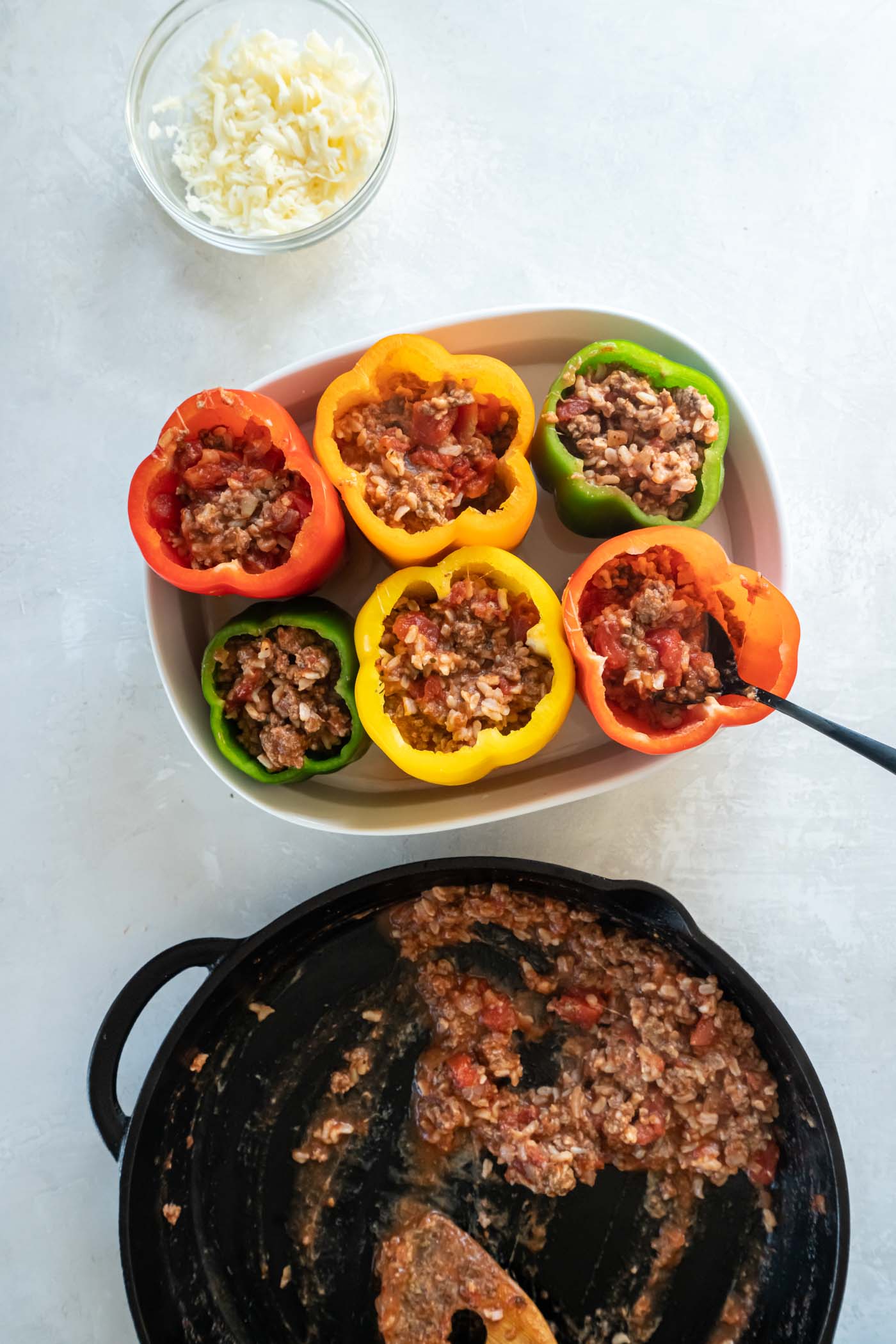 Spooning meat and rice filling into raw bell peppers.