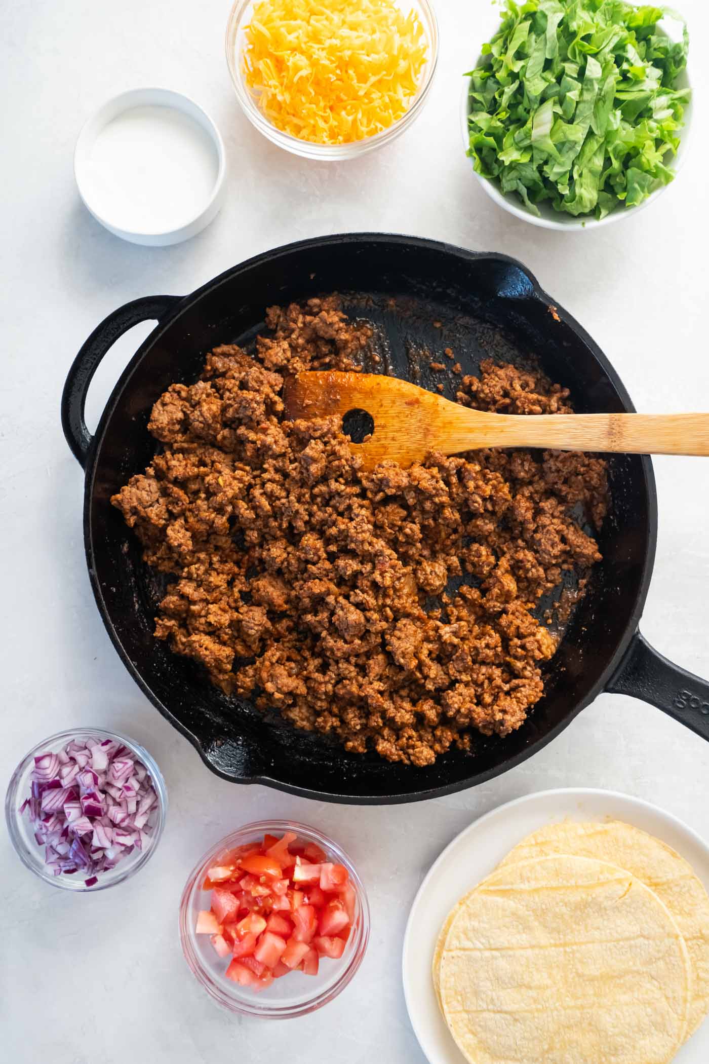 Taco meat in skillet with taco toppings in bowls.