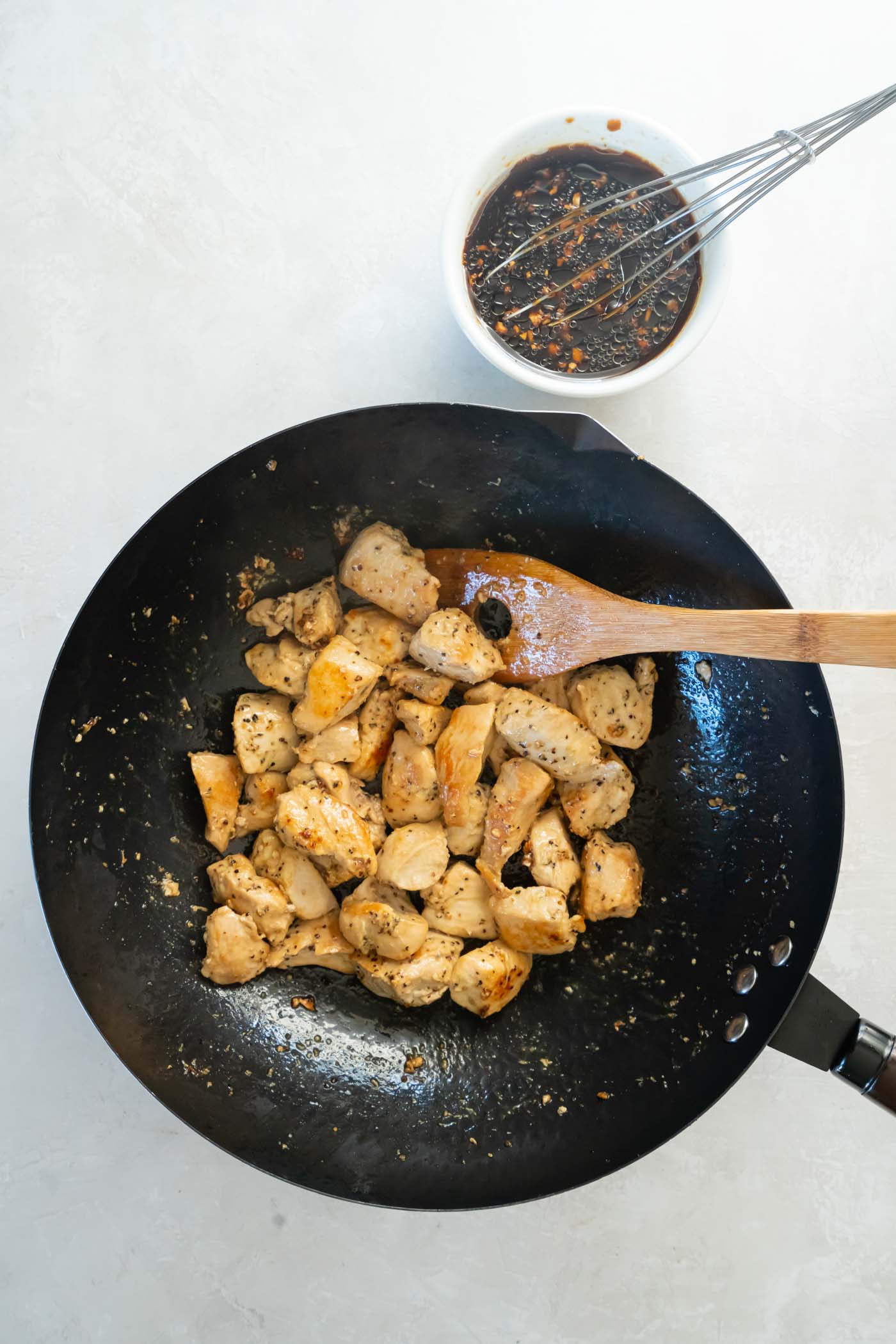 Browned chicken pieces in a skillet with a wooden spoon.