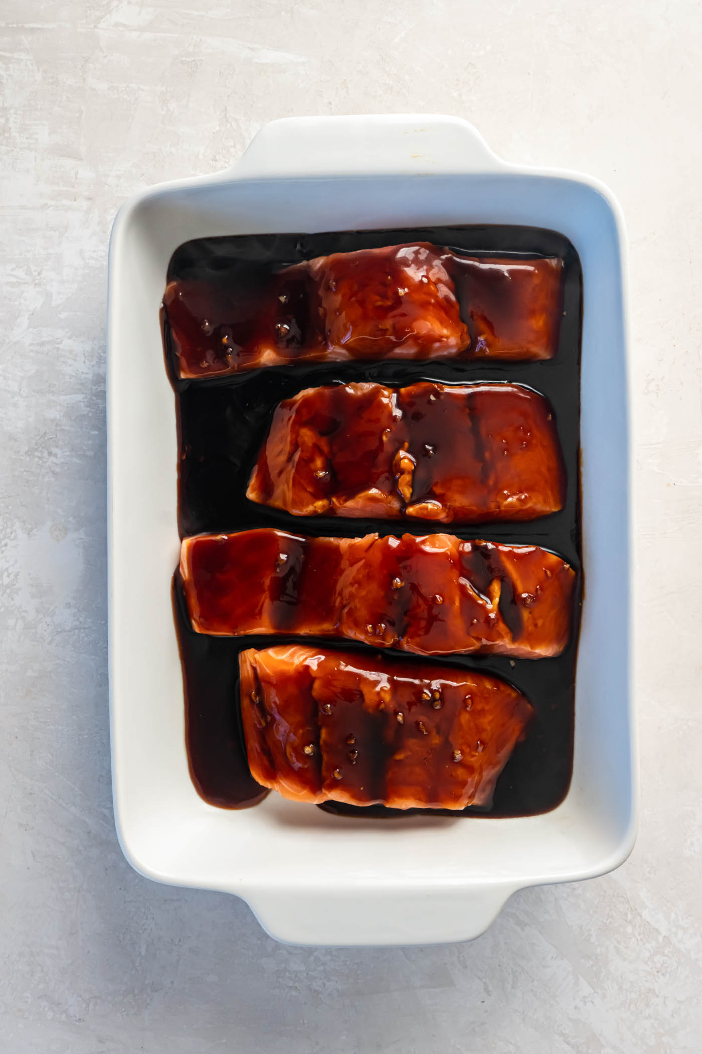 Teriyaki sauce poured over four salmon fillets in baking dish, before baking.