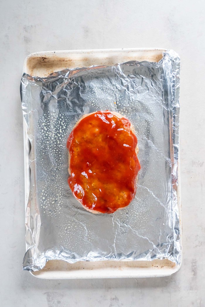 Uncooked turkey meatloaf with sauce on foil-lined baking sheet.
