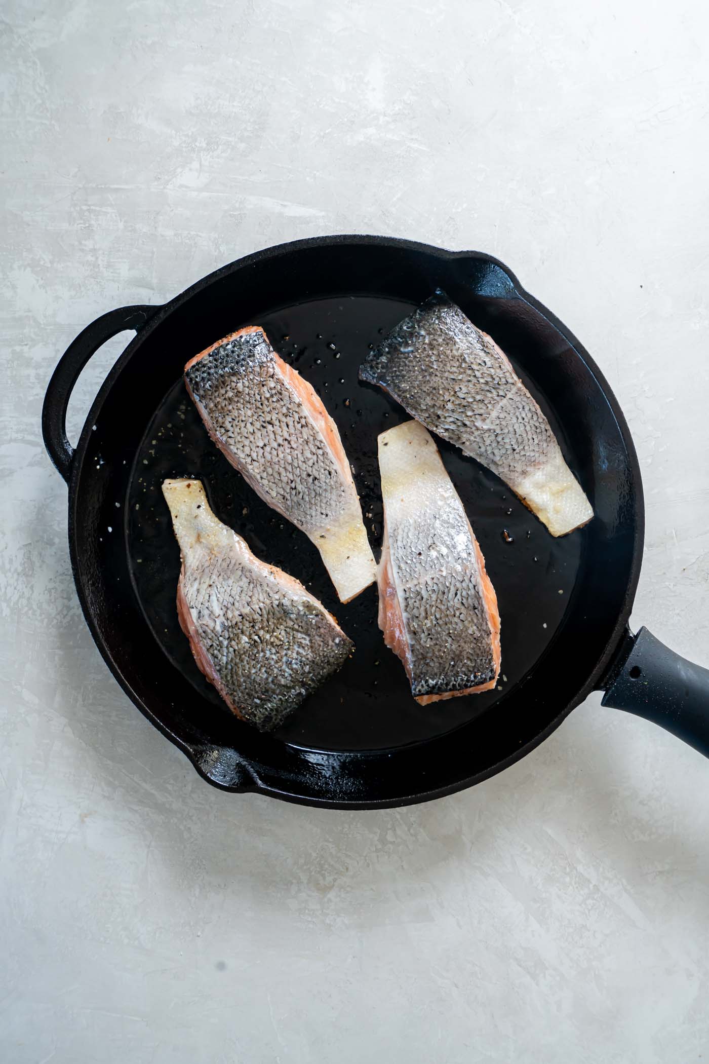Four salmon fillets in a skillet with the skin side up.