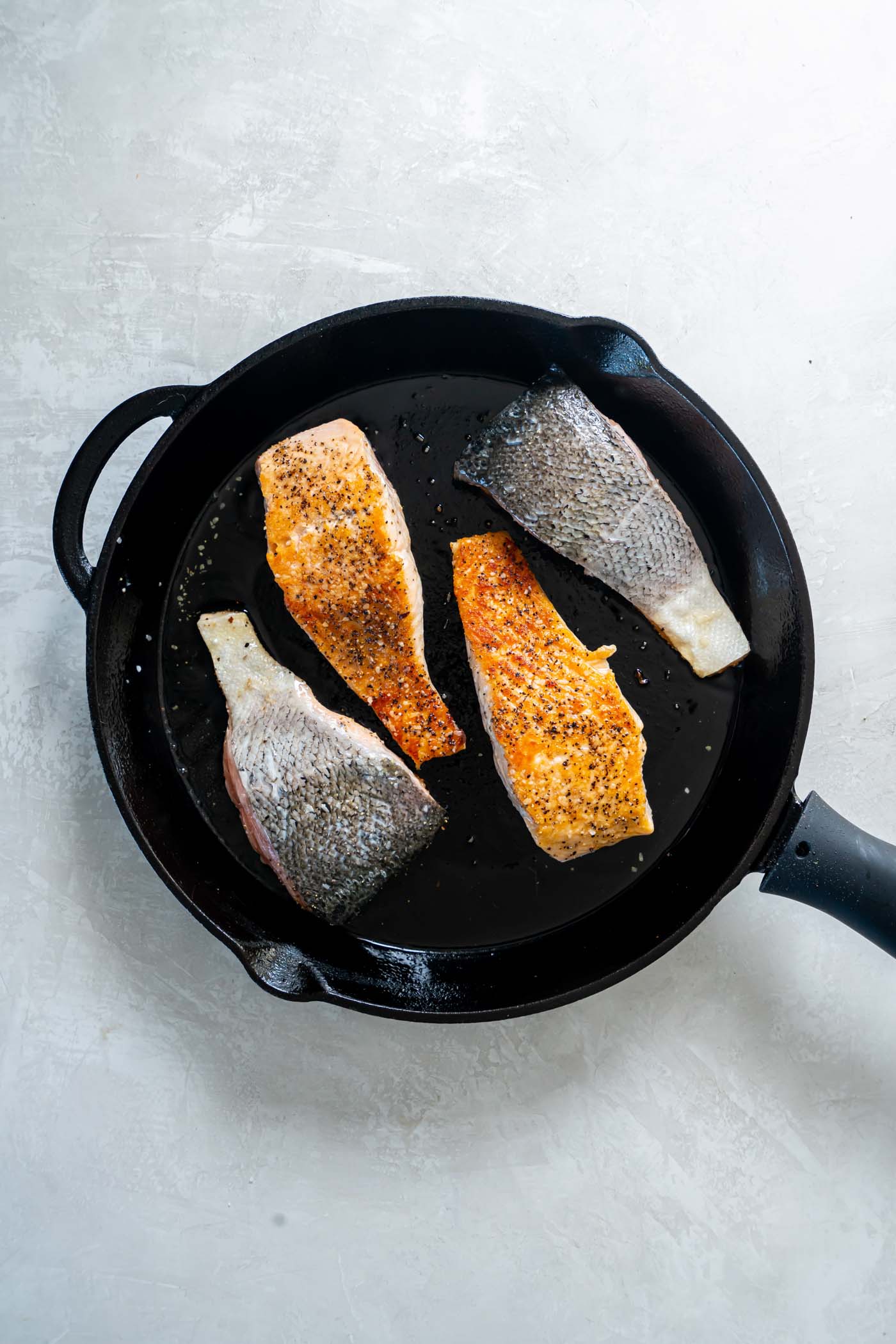 Four salmon fillets in a cast iron skillet with two skin side up and two flipped over skin side down.