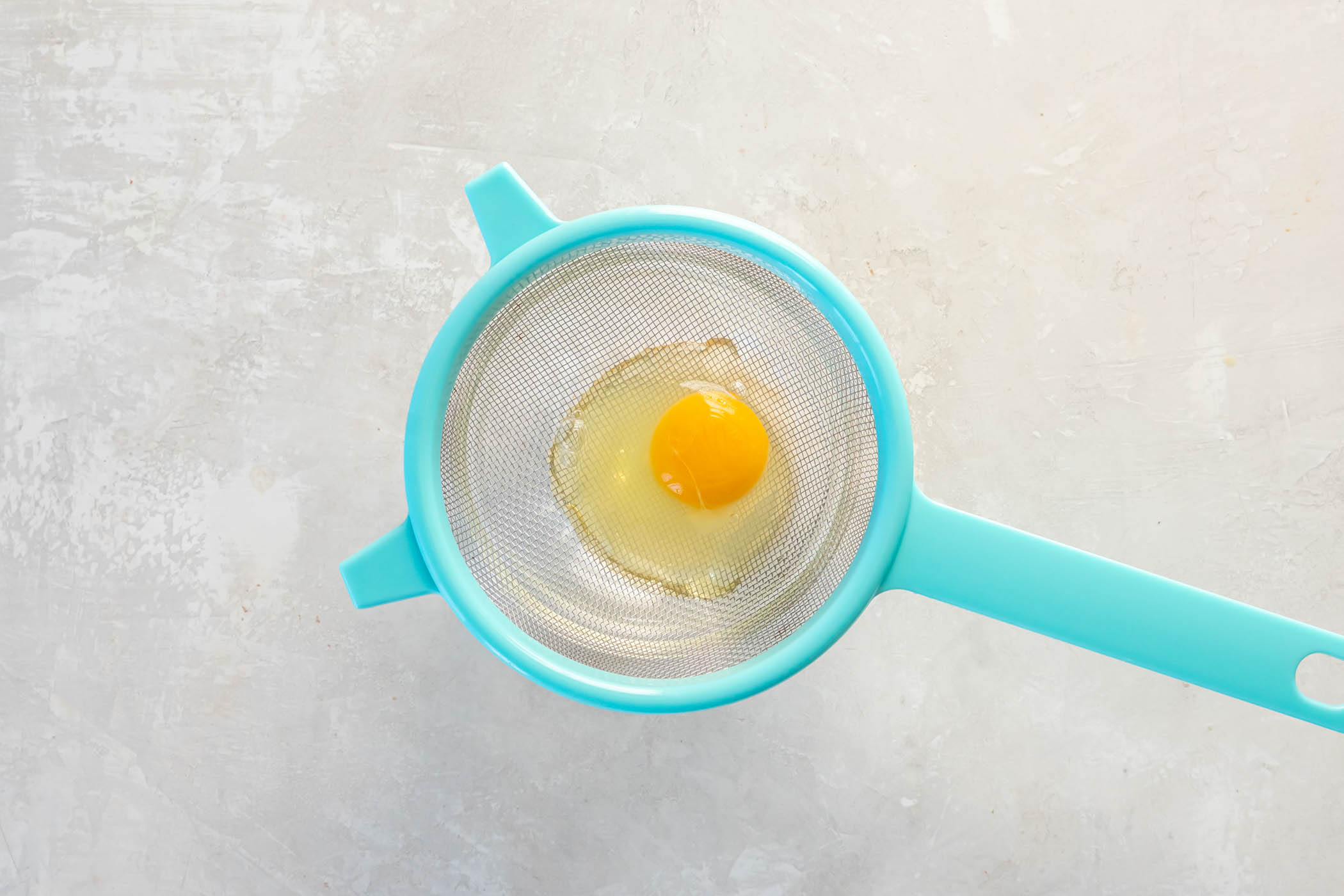 Egg cracked into a mesh strainer set over a bowl.