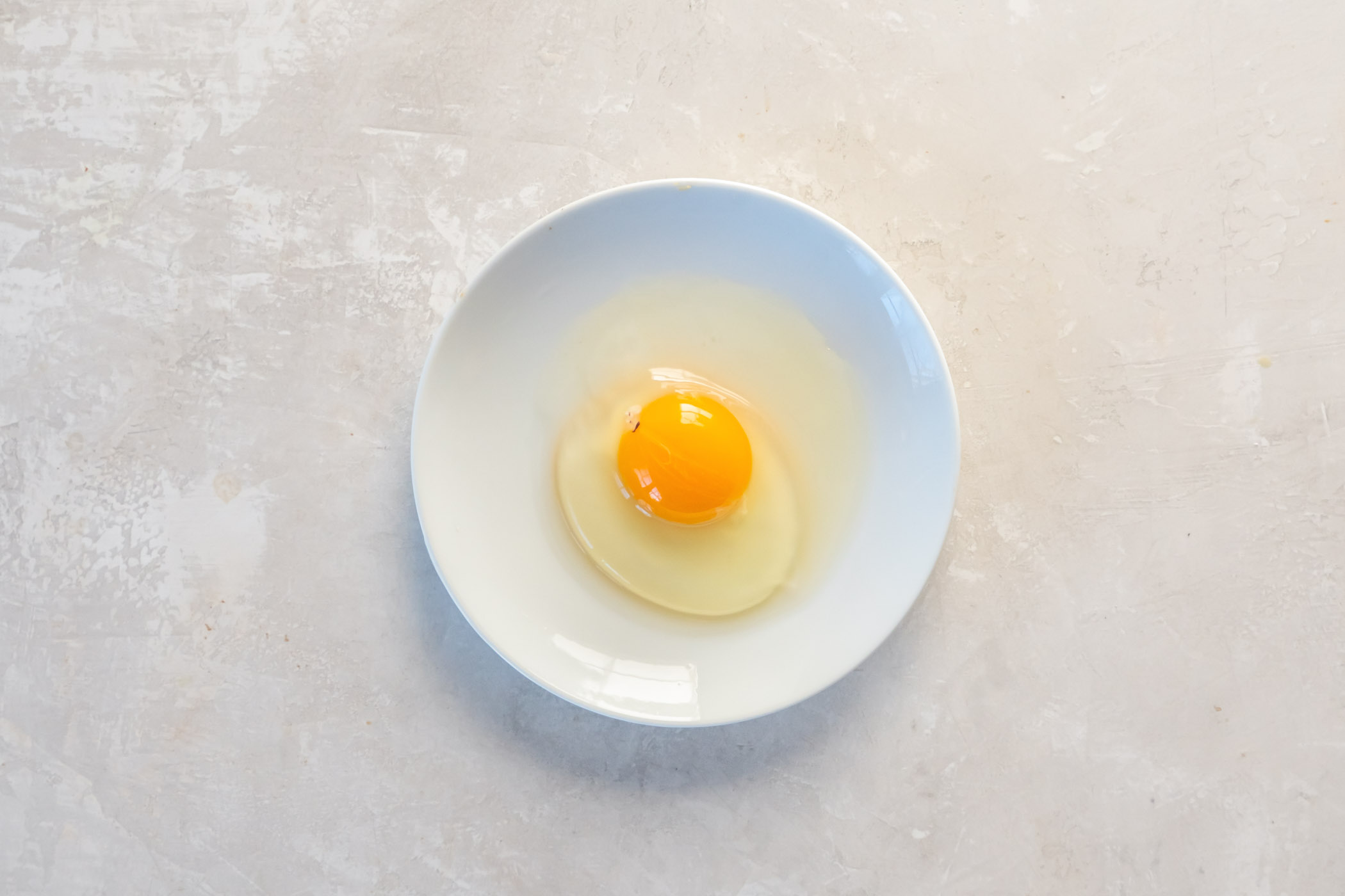 Egg cracked onto a plate showing firmer egg white and more watery egg white.